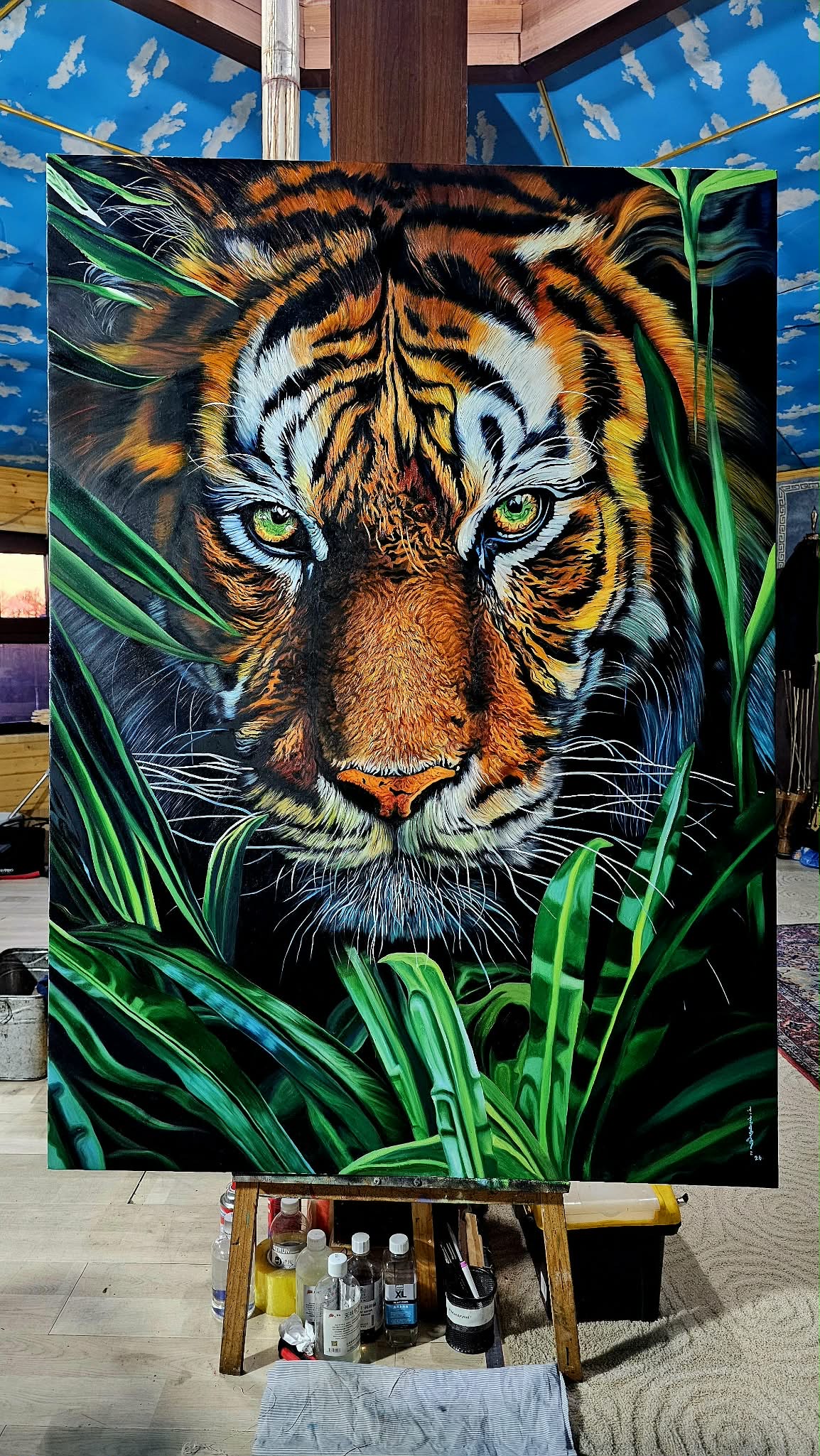 A person in a suit observes a large, hyper-realistic tiger painting amidst lush green foliage.
