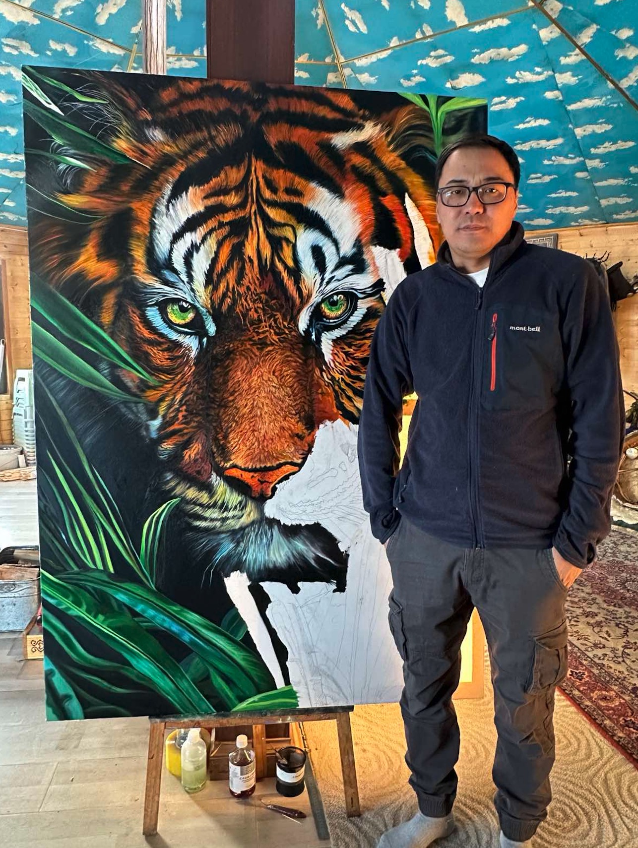 A person in a suit observes a large, hyper-realistic tiger painting amidst lush green foliage.