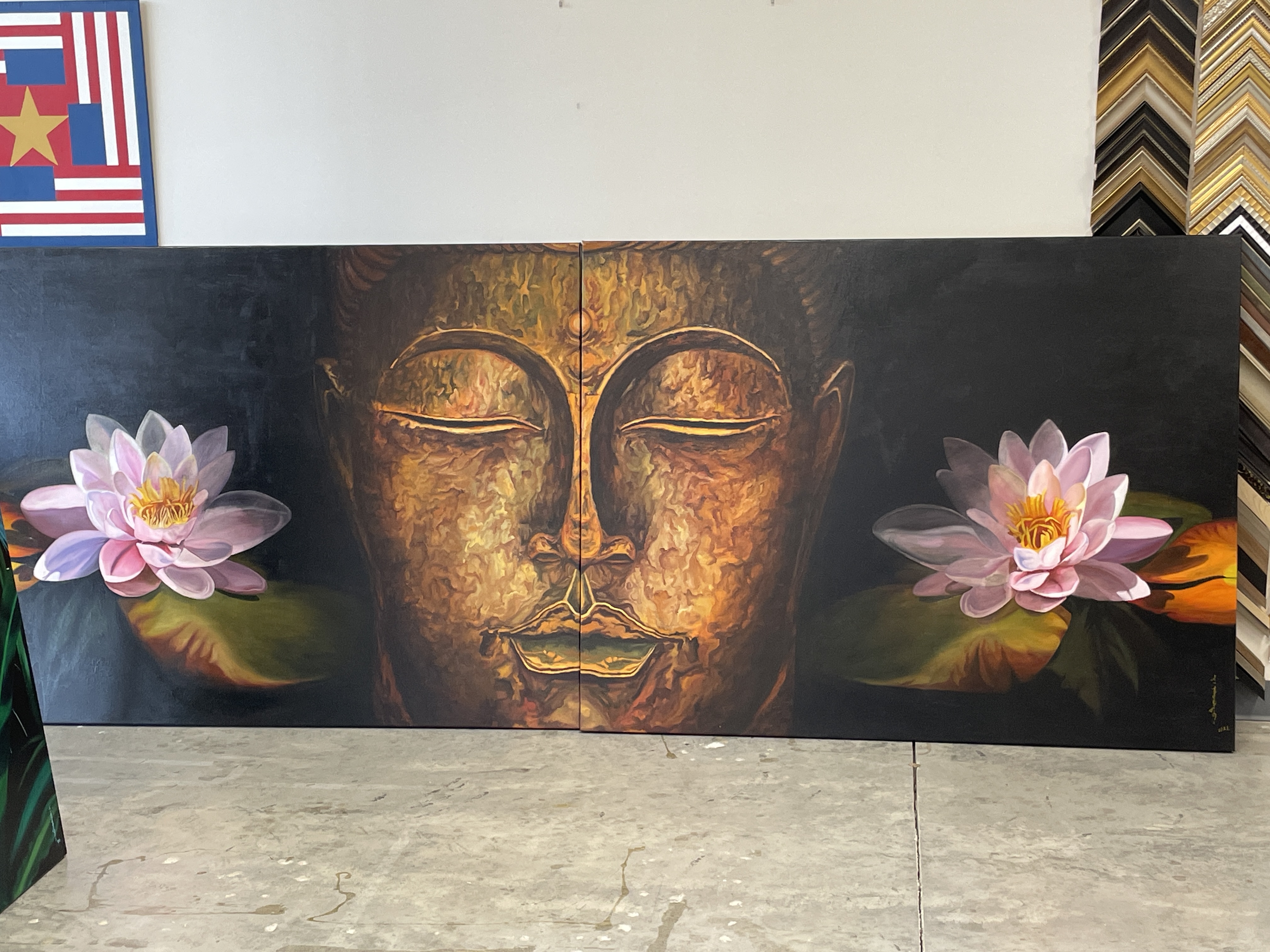 A person stands in a gallery, observing a large painting of a golden face flanked by pink lotus flowers.