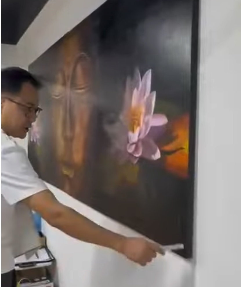 A person stands in a gallery, observing a large painting of a golden face flanked by pink lotus flowers.