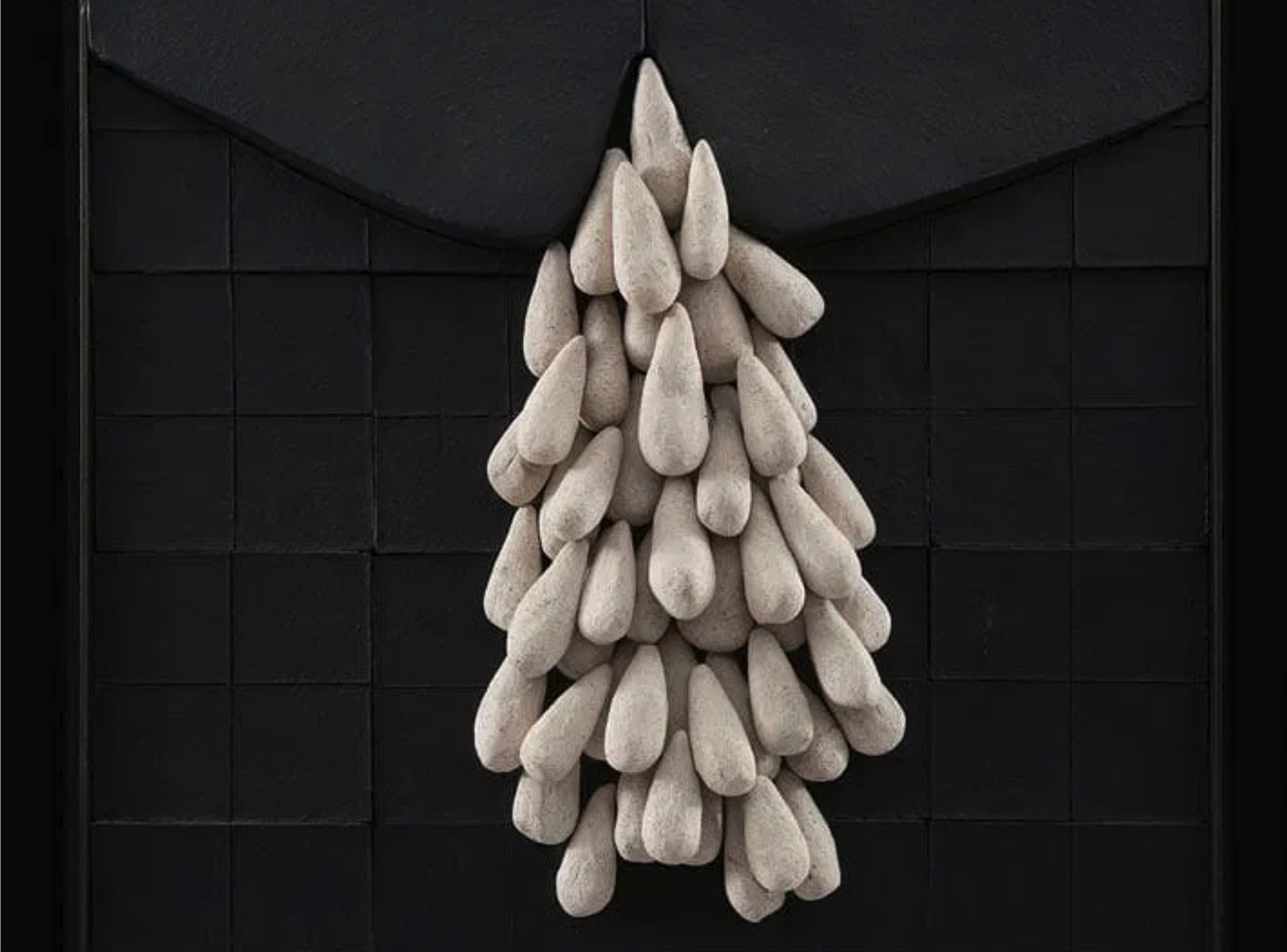 A sculptural composition featuring a cluster of teardrop shapes emerging from a dark, grid-like surface.