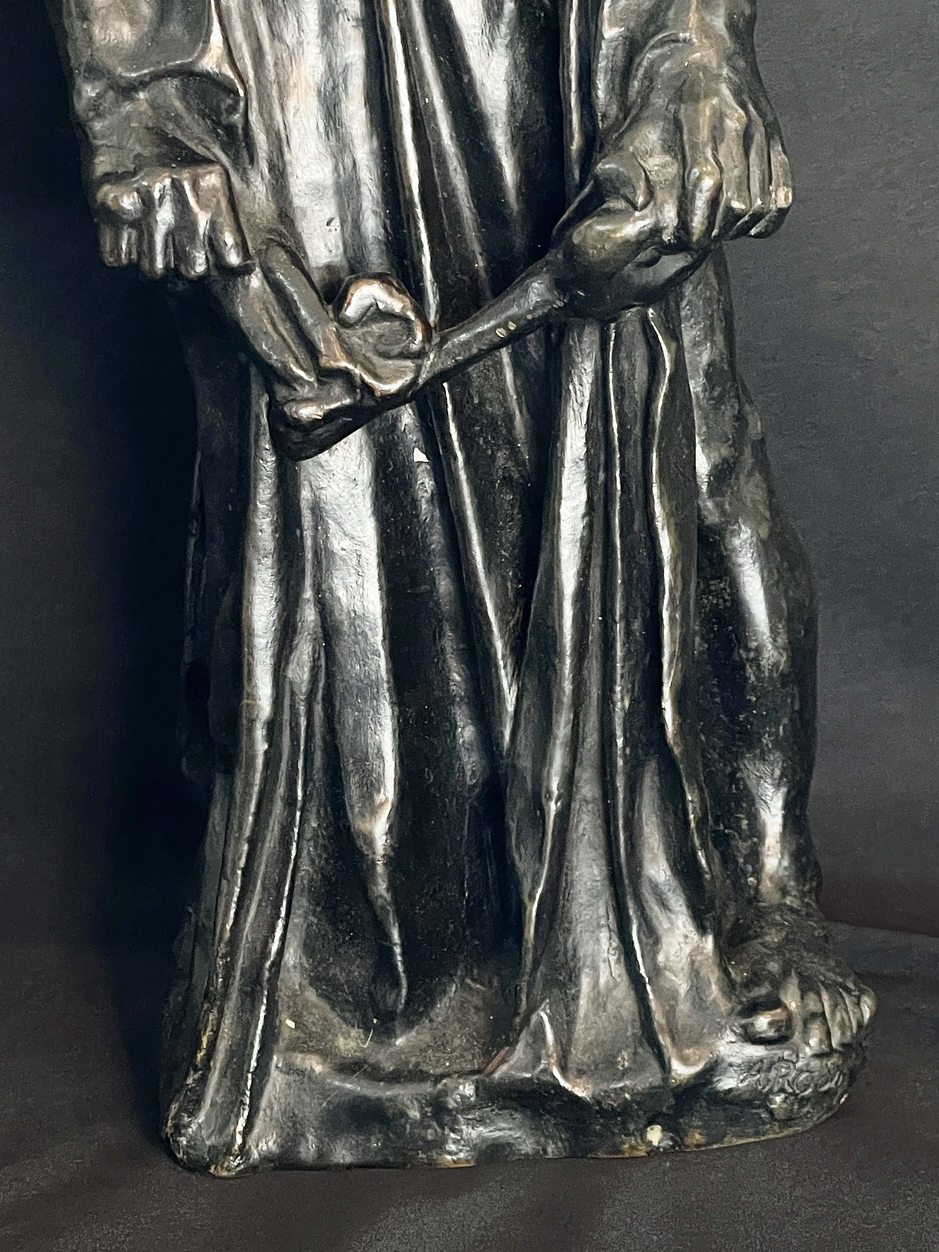 A museum display featuring a bronze statue, framed portraits, and an old book.