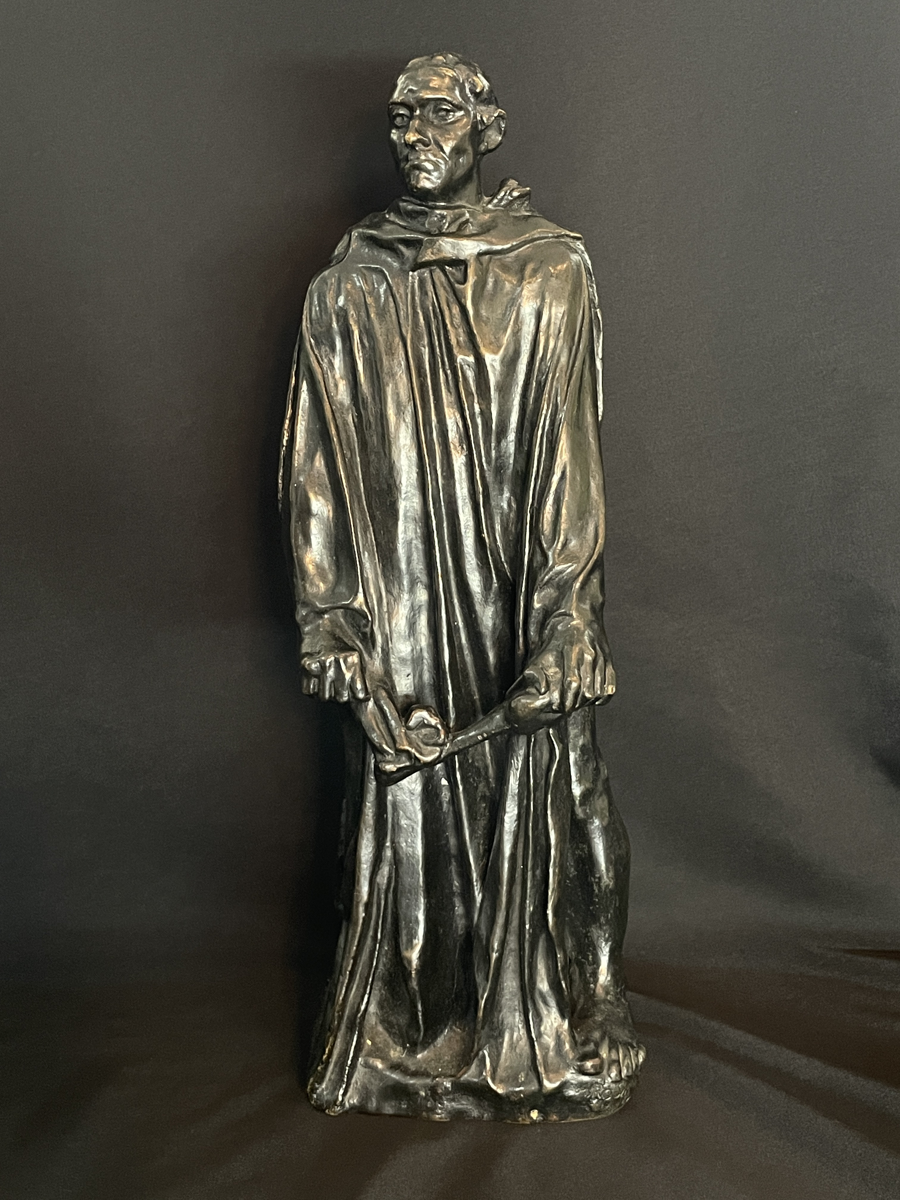 A museum display featuring a bronze statue, framed portraits, and an old book.
