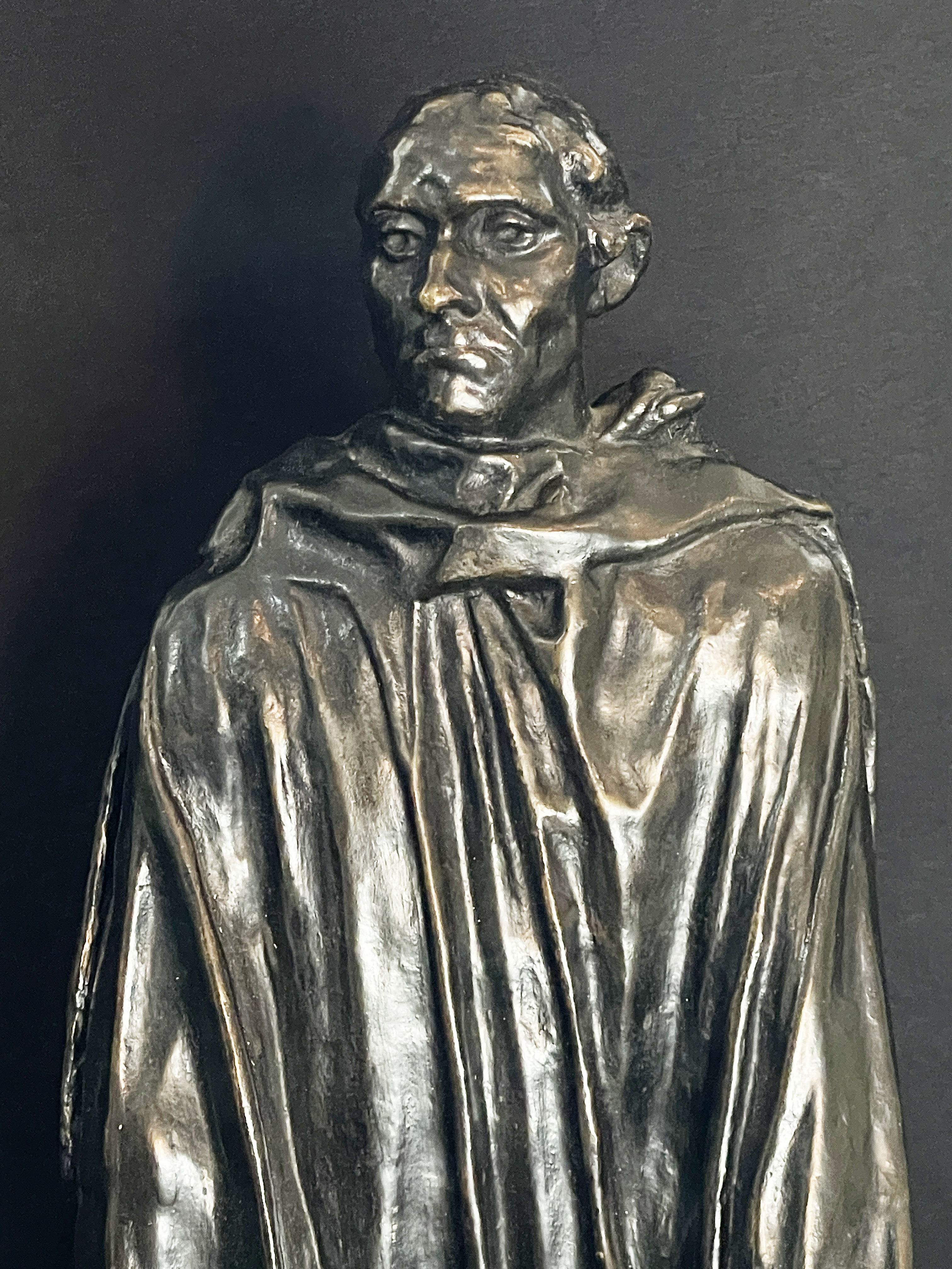 A museum display featuring a bronze statue, framed portraits, and an old book.