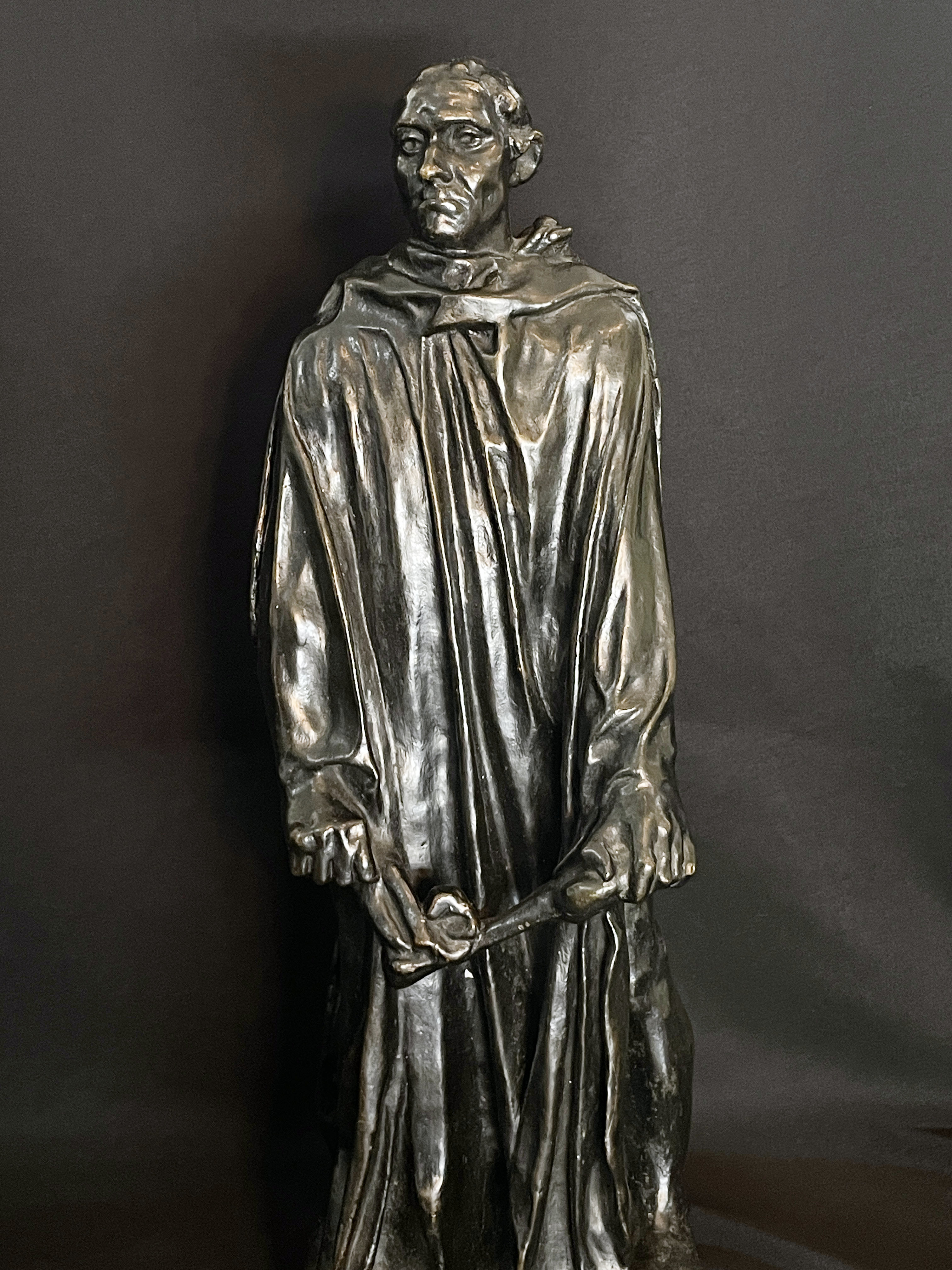 A museum display featuring a bronze statue, framed portraits, and an old book.