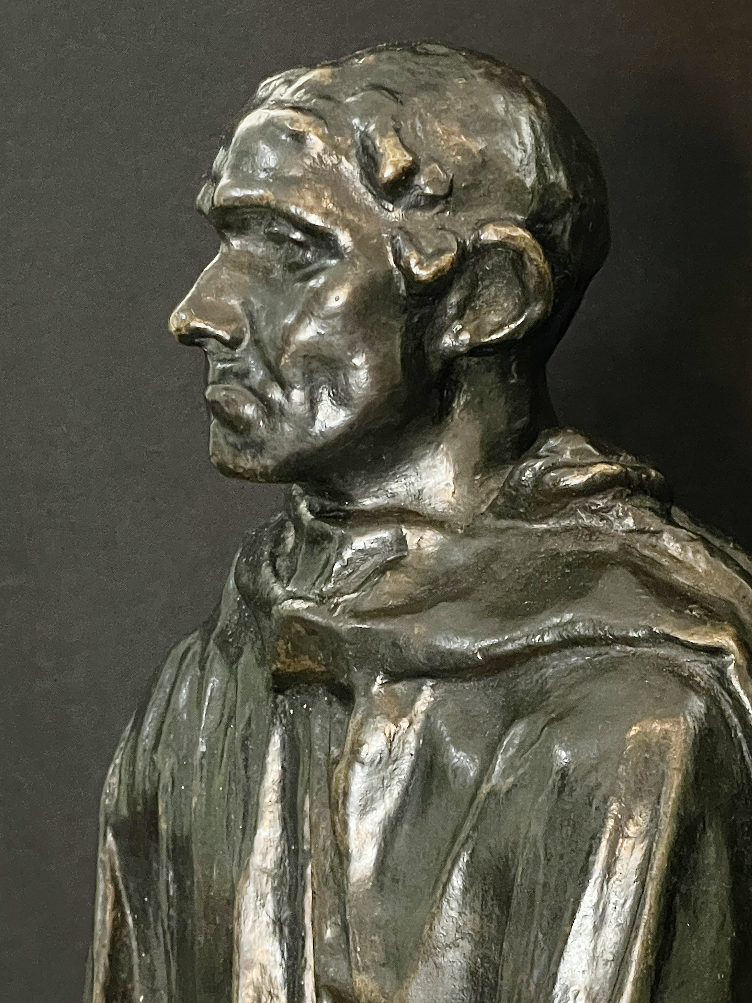 A museum display featuring a bronze statue, framed portraits, and an old book.