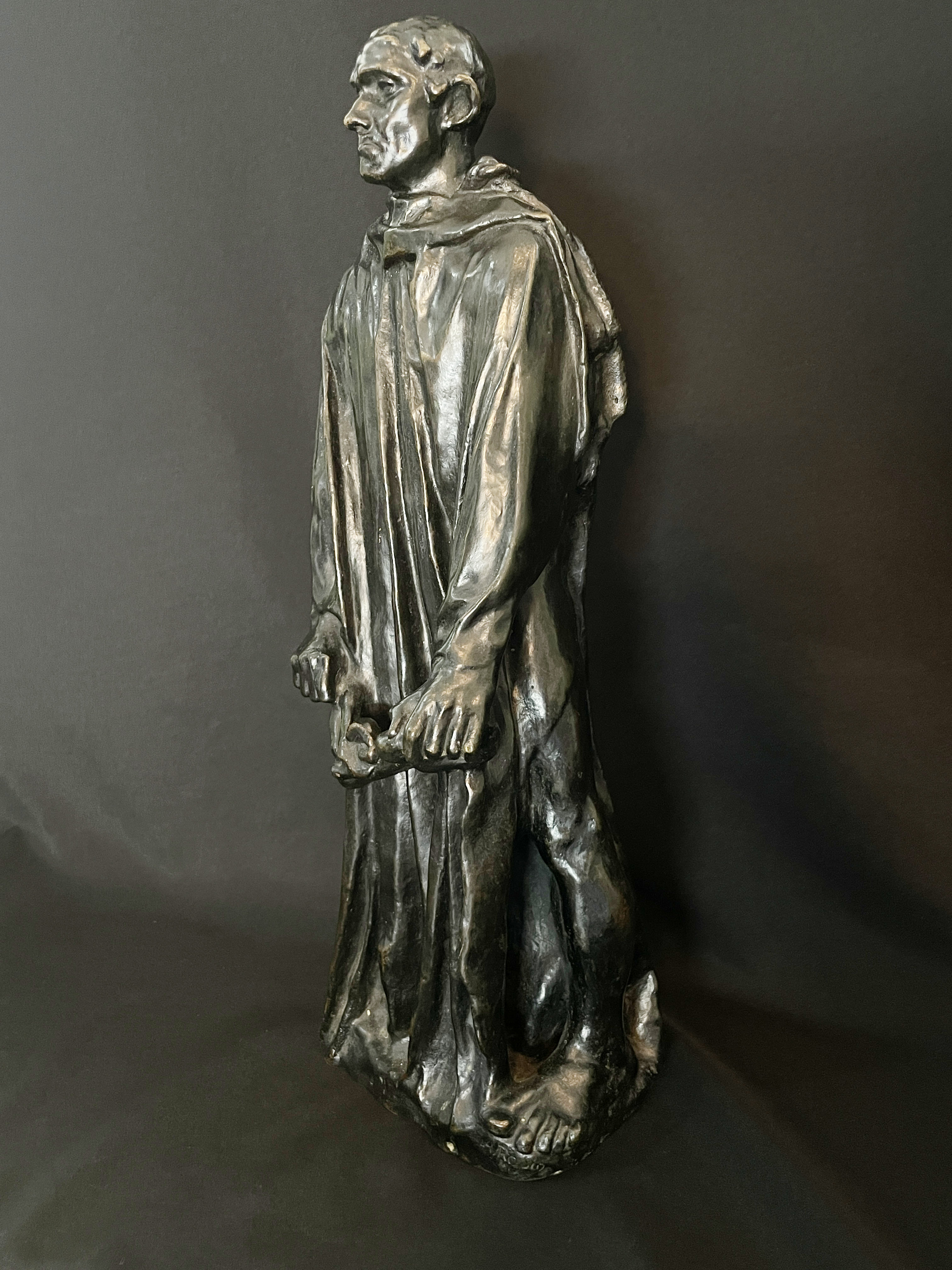 A museum display featuring a bronze statue, framed portraits, and an old book.