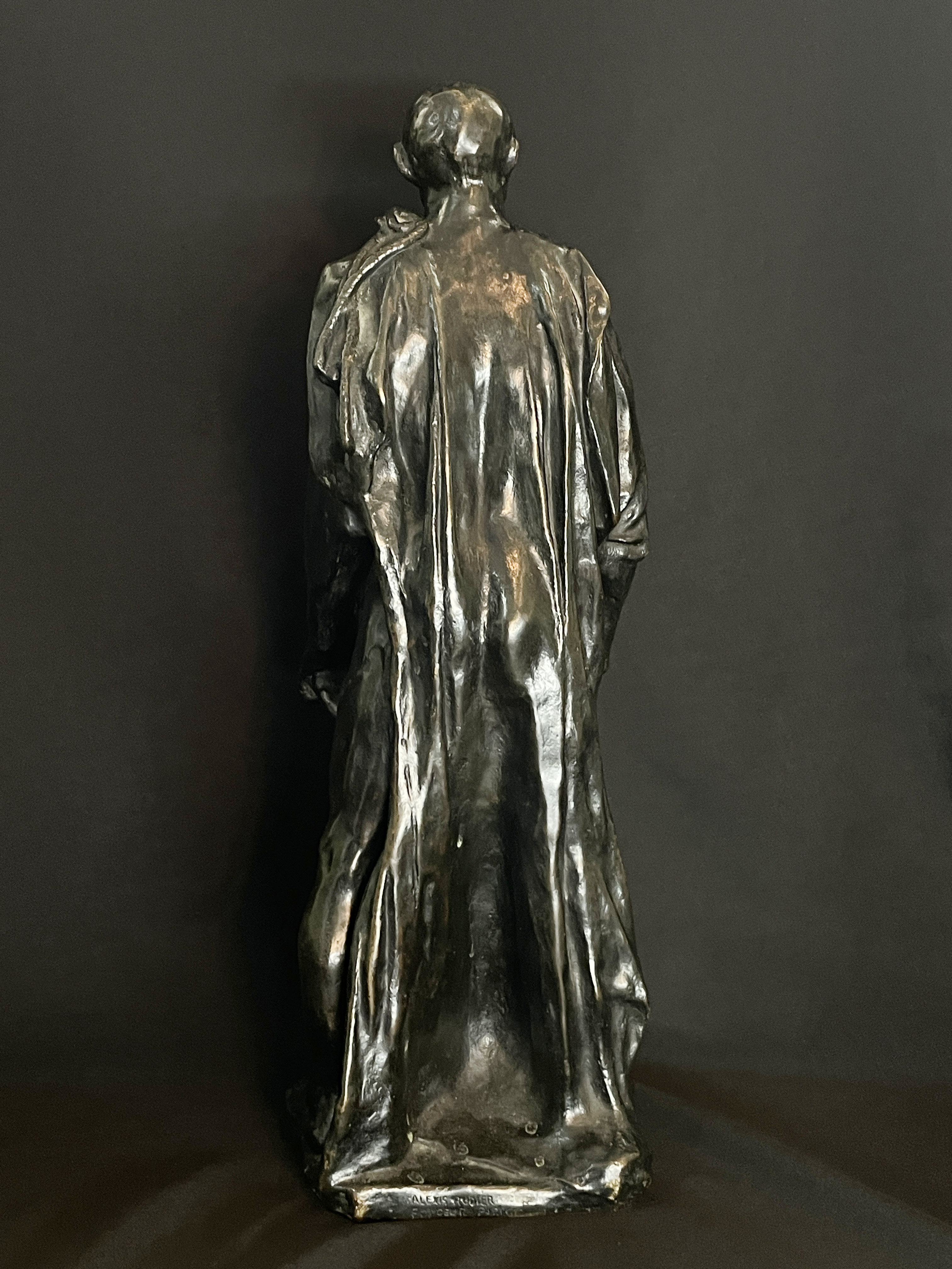 A museum display featuring a bronze statue, framed portraits, and an old book.