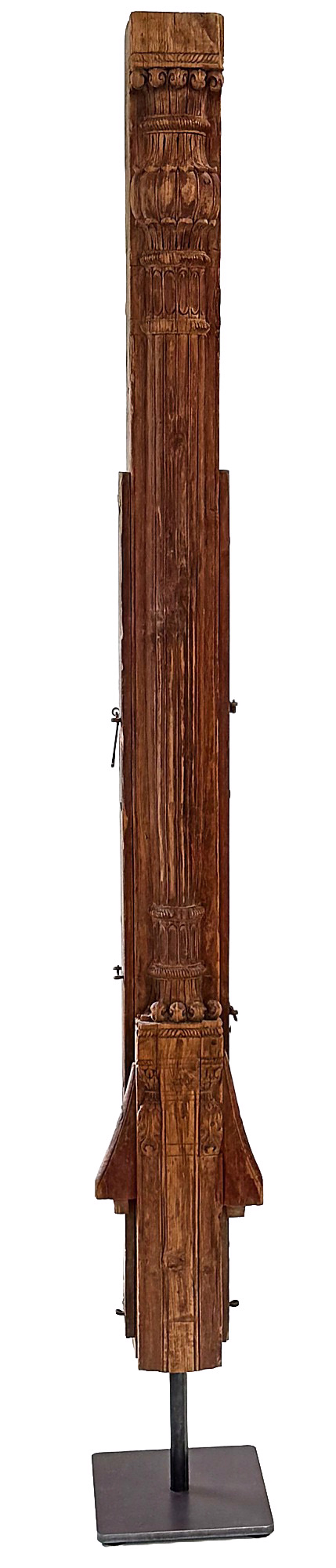 A wooden sculpture of a tall wooden column on a metal stand.