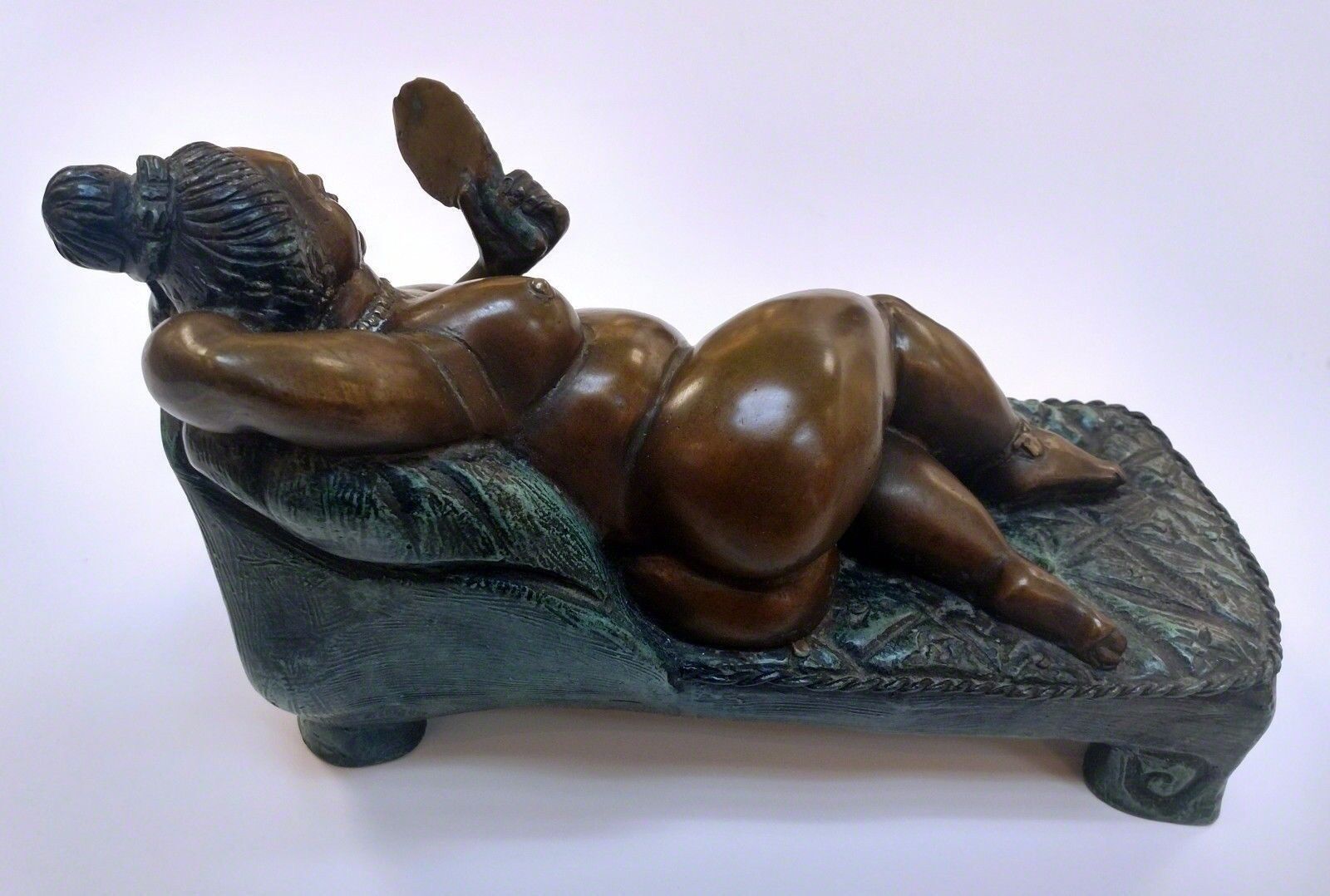 A bronze statue of a woman laying on a couch.