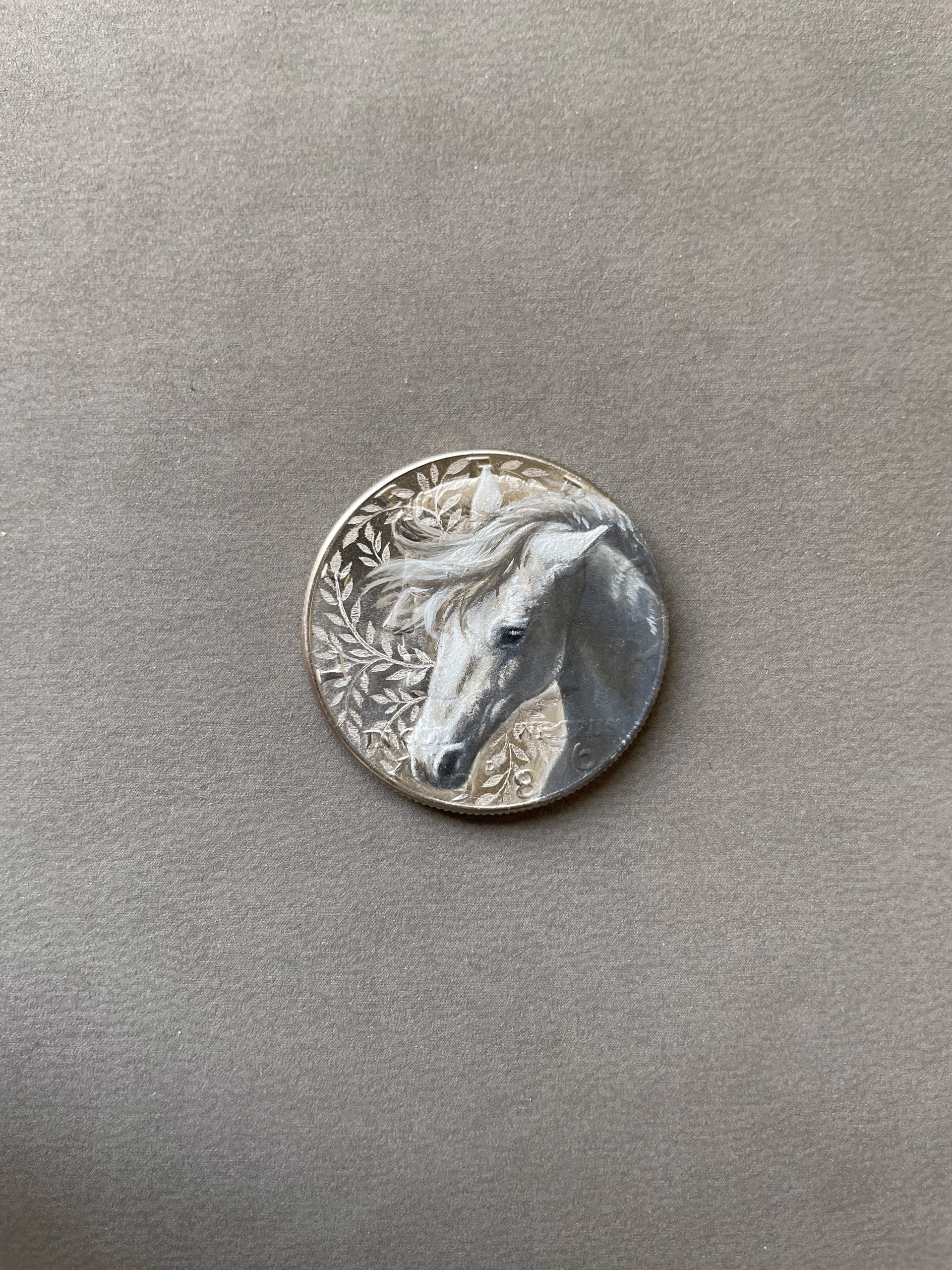A silver coin with a white horse head on it.