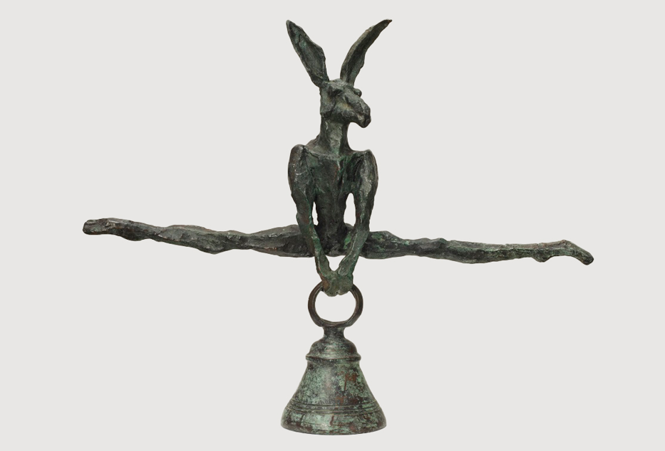 A bronze sculpture of a hare balancing on a ring atop a bell.