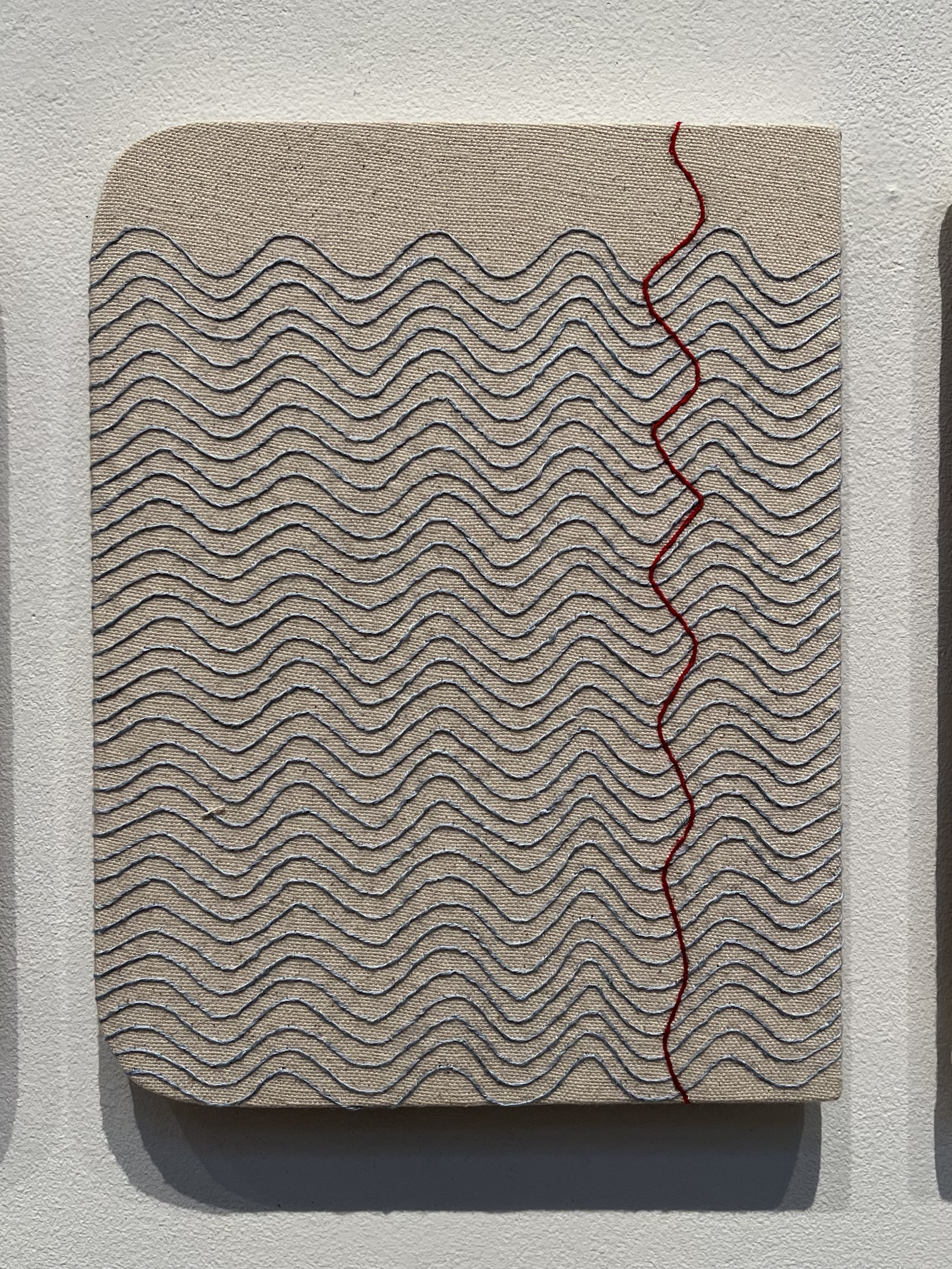 A piece of art hanging on a wall with a red line on it.