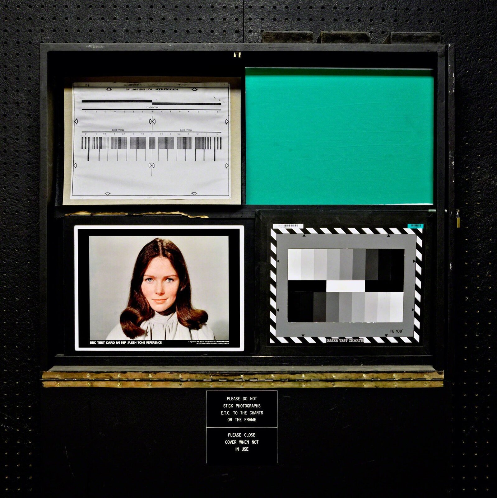 A black display case containing a framed portrait, color test charts, and technical reference materials.