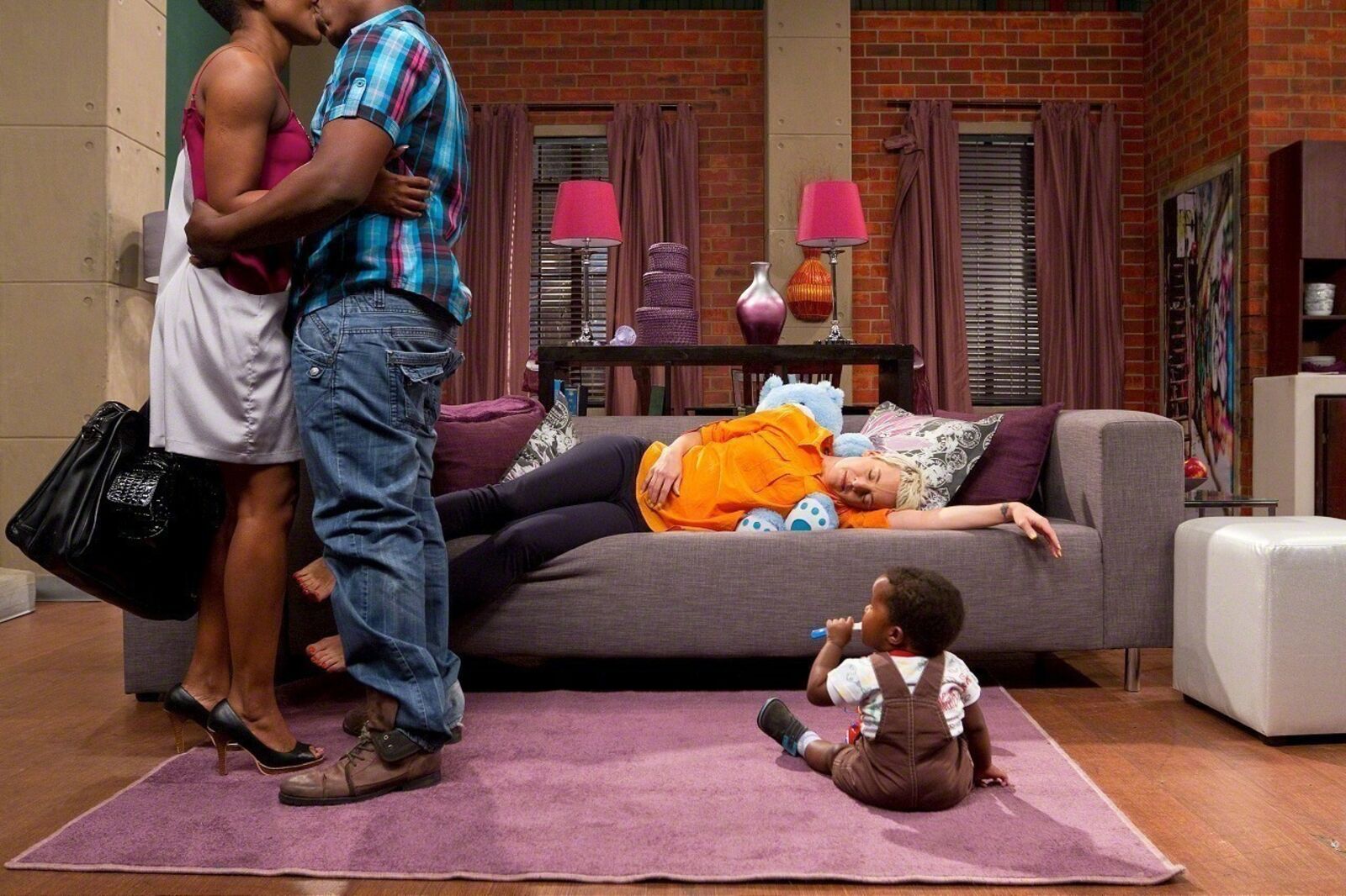A man and woman kissing a baby on a couch in a living room.
