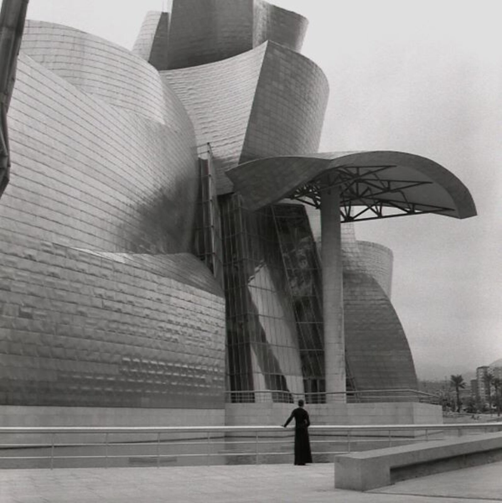 A black and white photo of a man standing in front of a building.