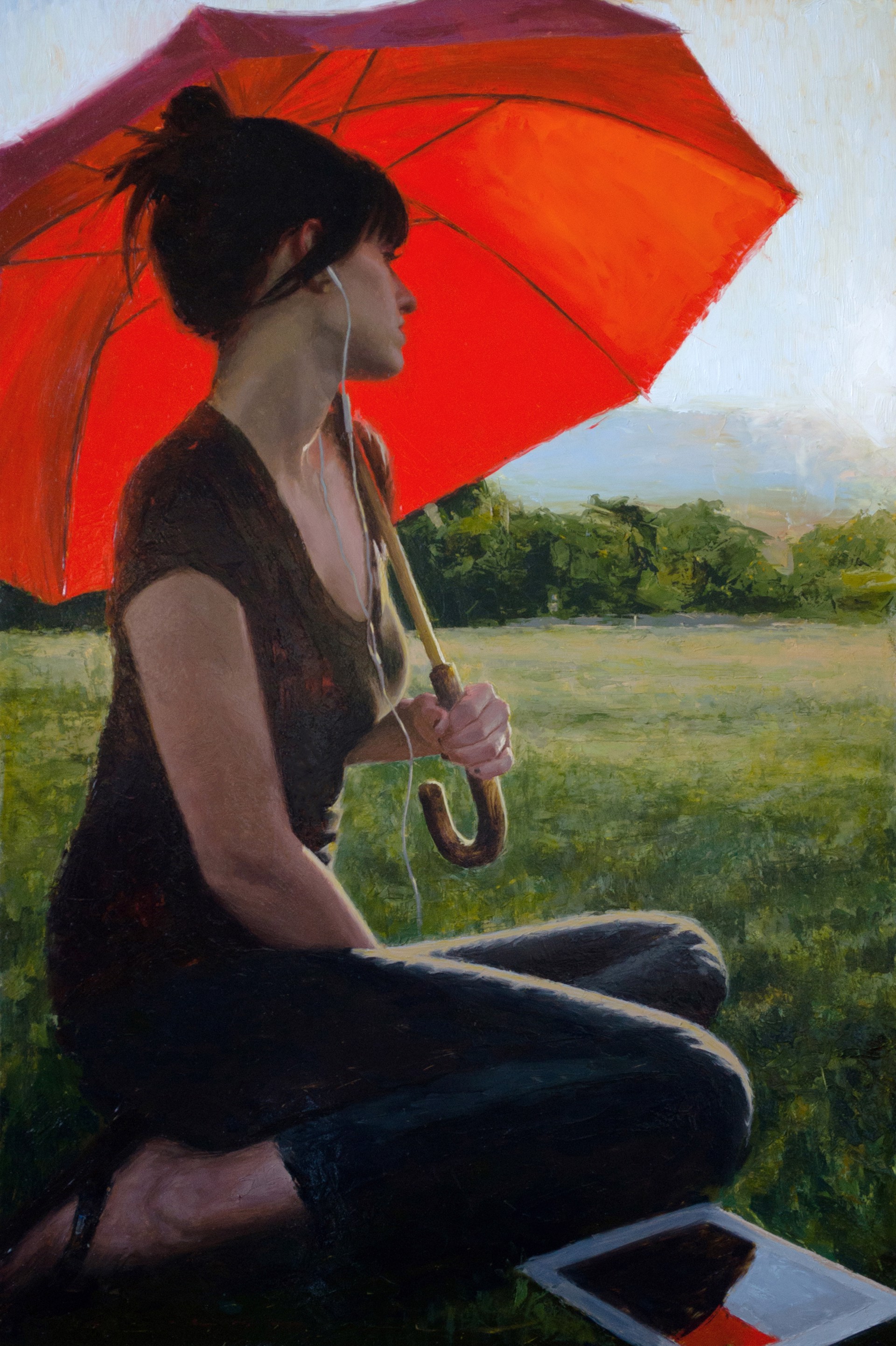 A person sits in a field under a large red umbrella, listening to music with earphones.