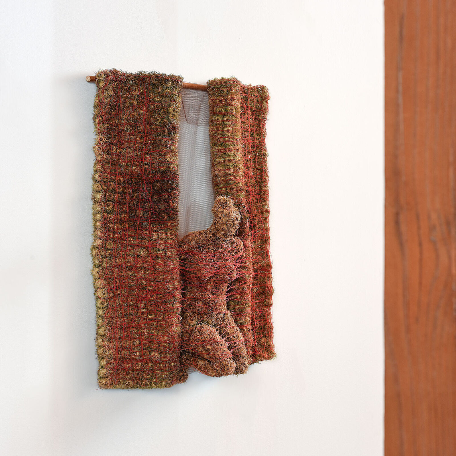 A piece of art hanging on a wall next to a wooden pole.
