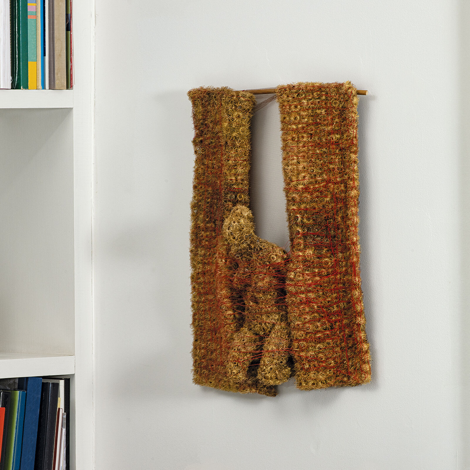 A piece of art hanging on a wall next to a wooden pole.
