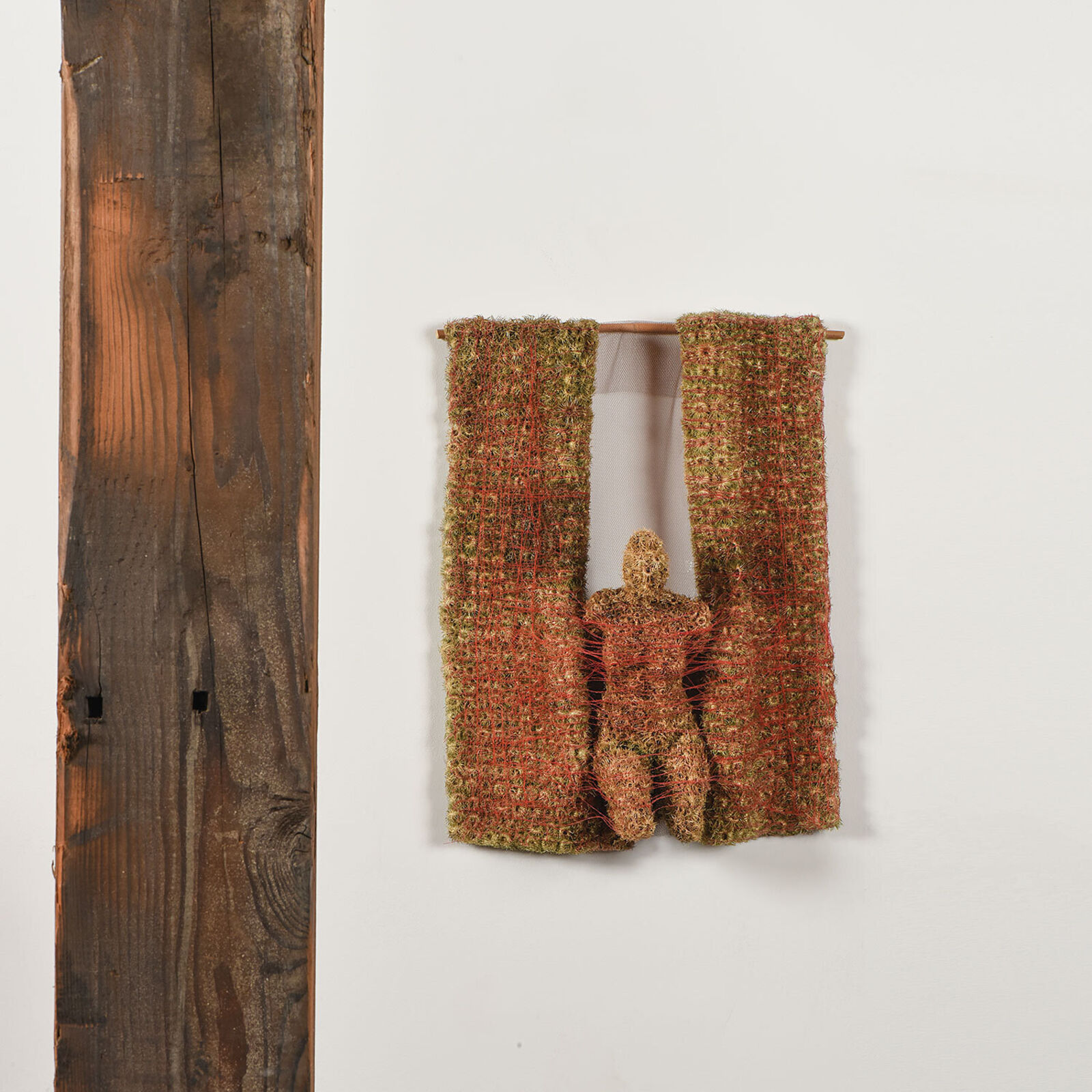 A piece of art hanging on a wall next to a wooden pole.