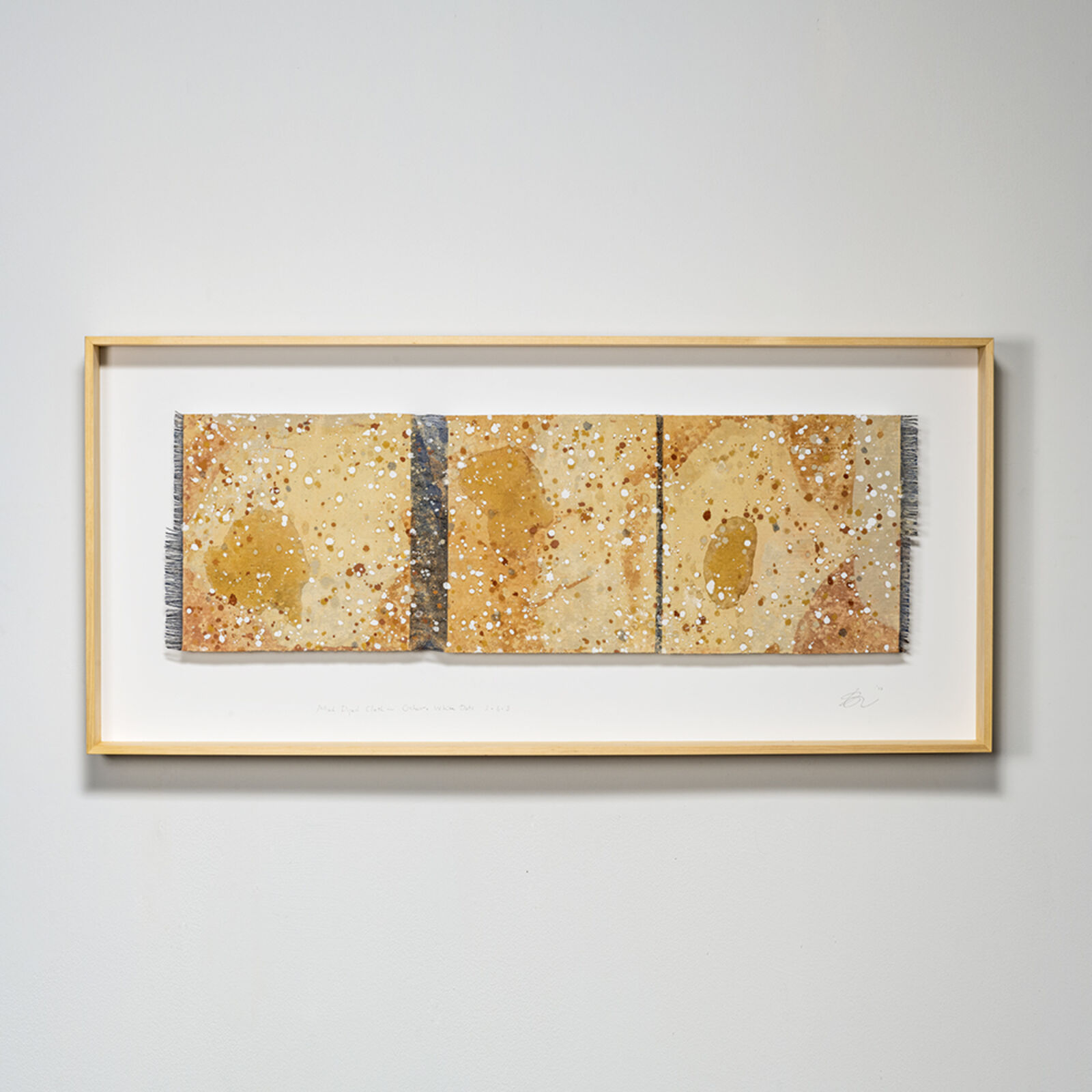 A framed textile artwork featuring a horizontal composition of earthy tones, speckled patterns, and vertical dividers.