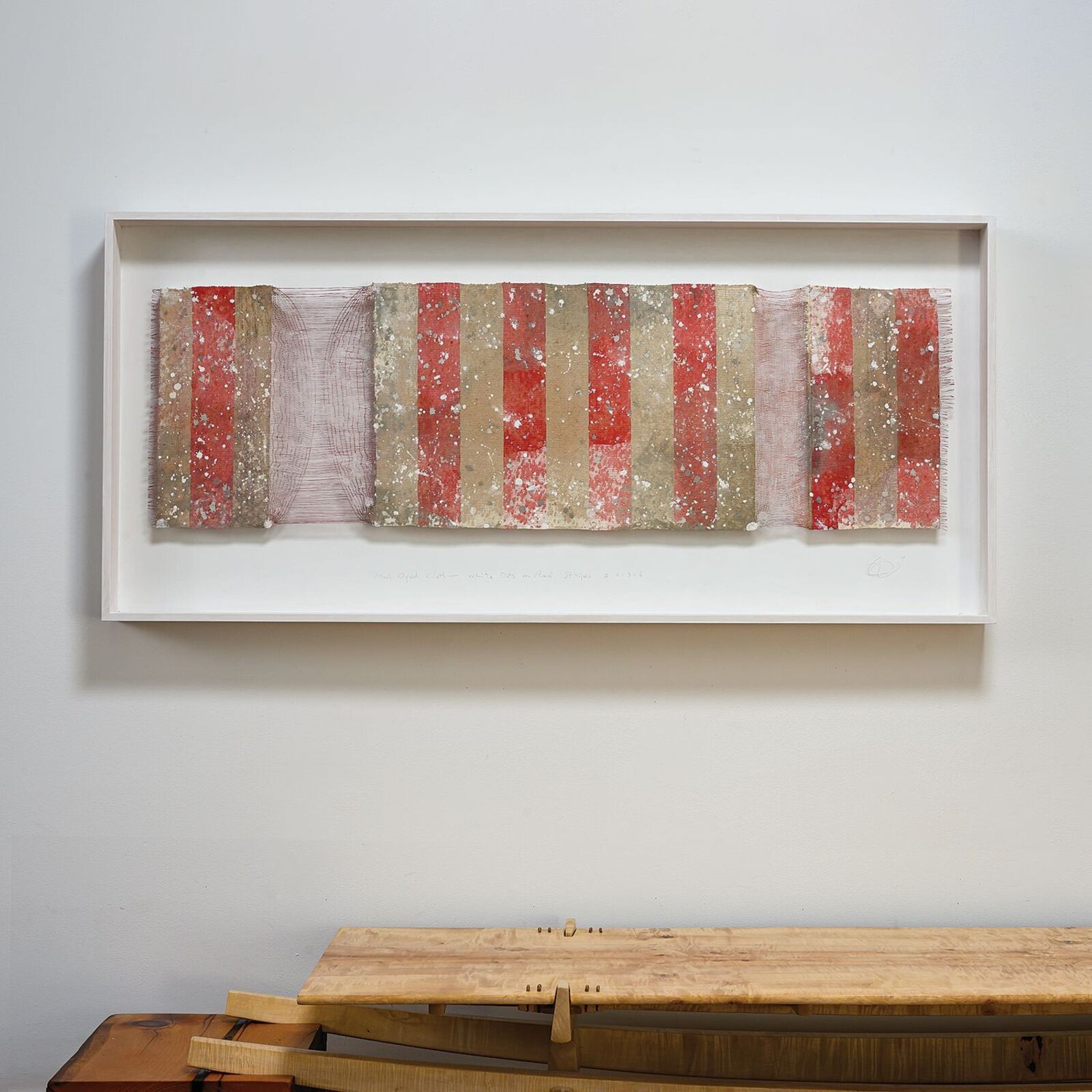 A framed textile artwork featuring vertical red and beige stripes with a weathered, speckled texture.