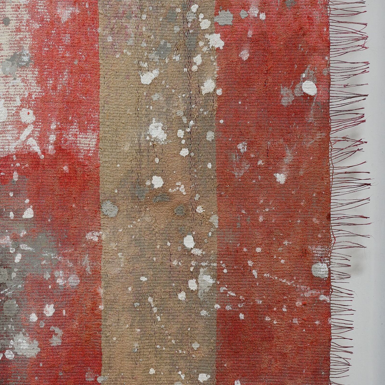 A framed textile artwork featuring vertical red and beige stripes with a weathered, speckled texture.