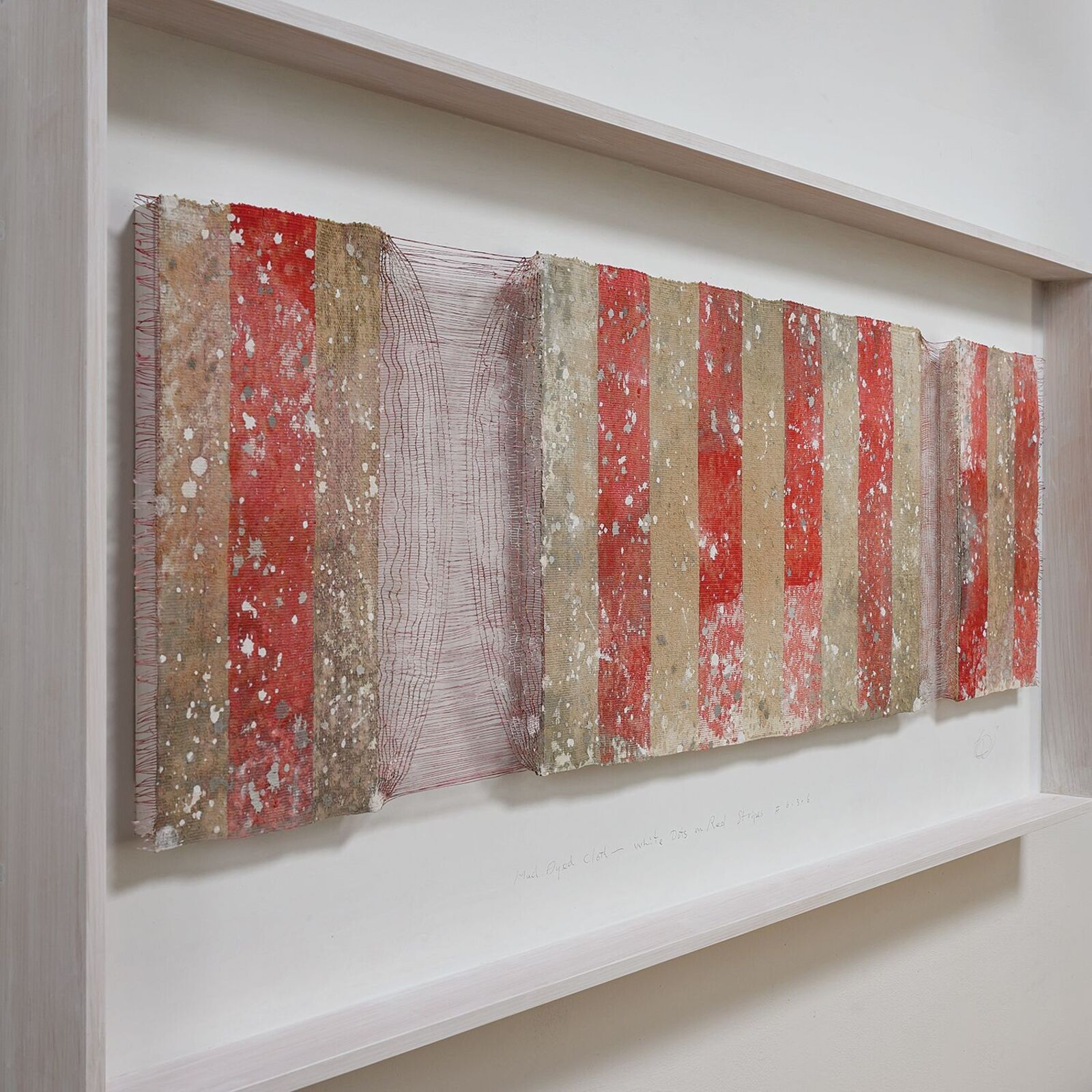 A framed textile artwork featuring vertical red and beige stripes with a weathered, speckled texture.