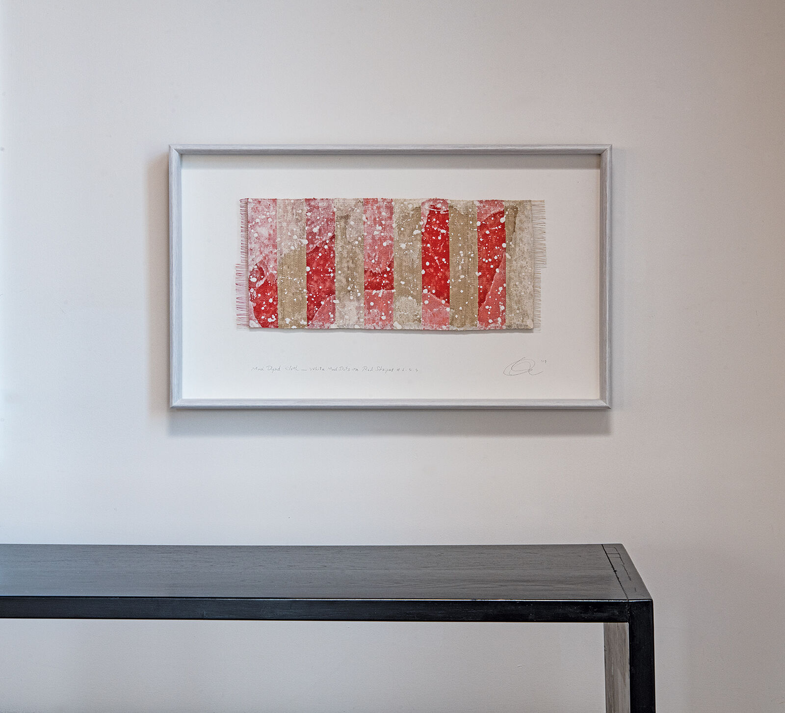 A framed textile artwork with vertical red and beige stripes hangs above a dark console table.
