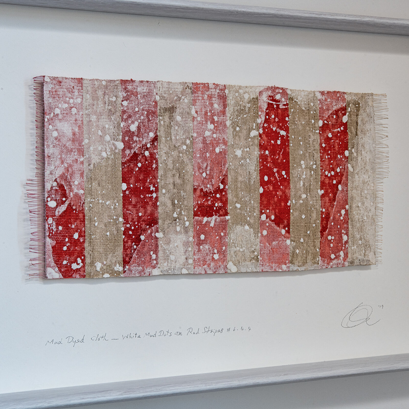 A framed textile artwork with vertical red and beige stripes hangs above a dark console table.