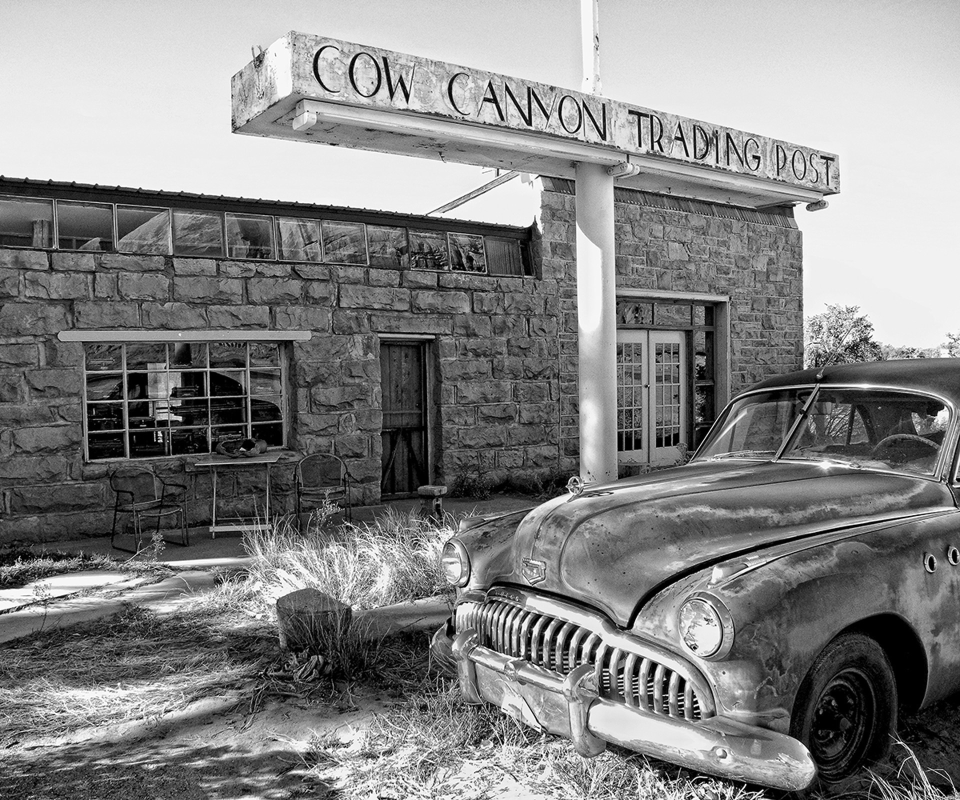A black and white photo of an old car parked in front of a building.