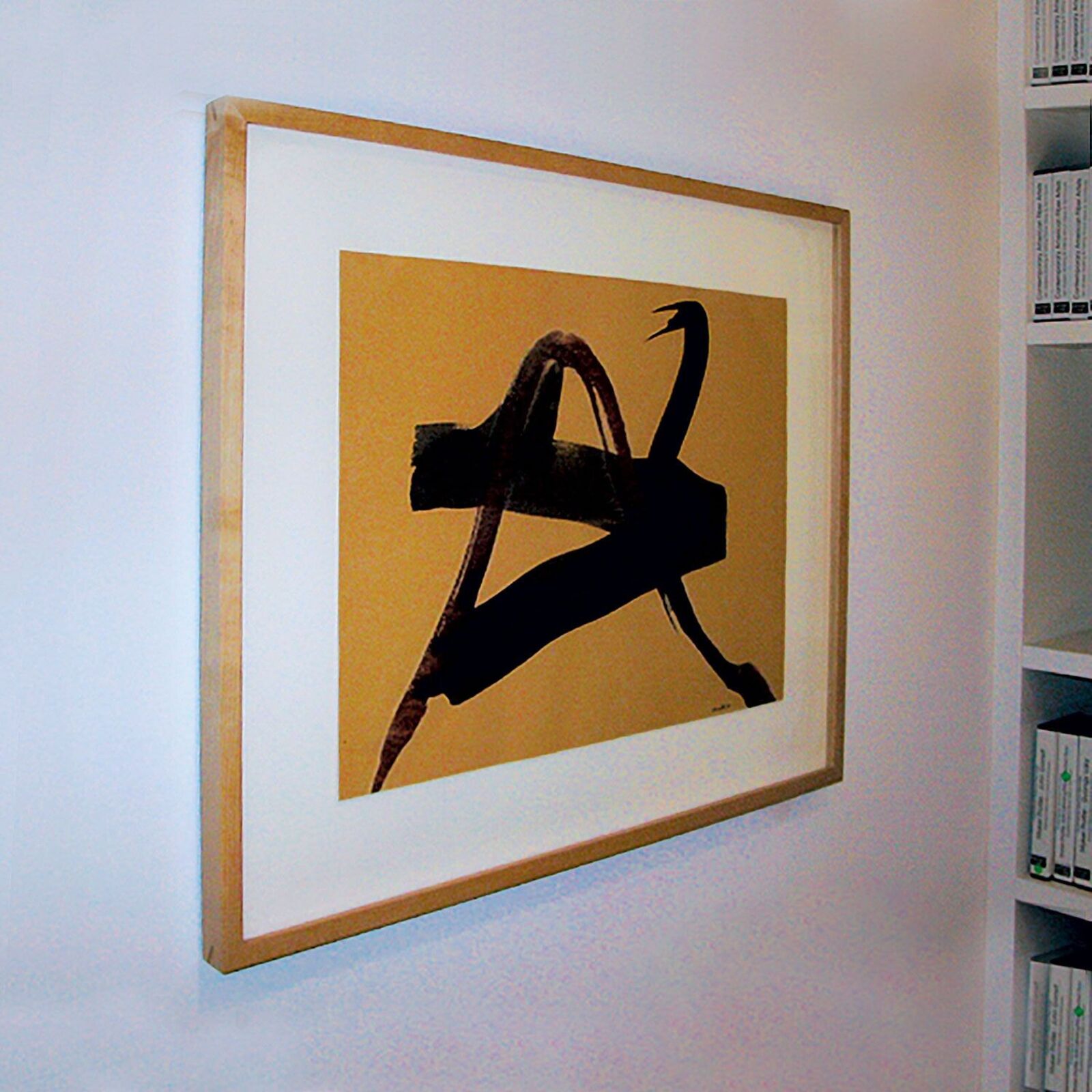 A framed abstract print featuring bold black brushstrokes on a mustard-yellow background.