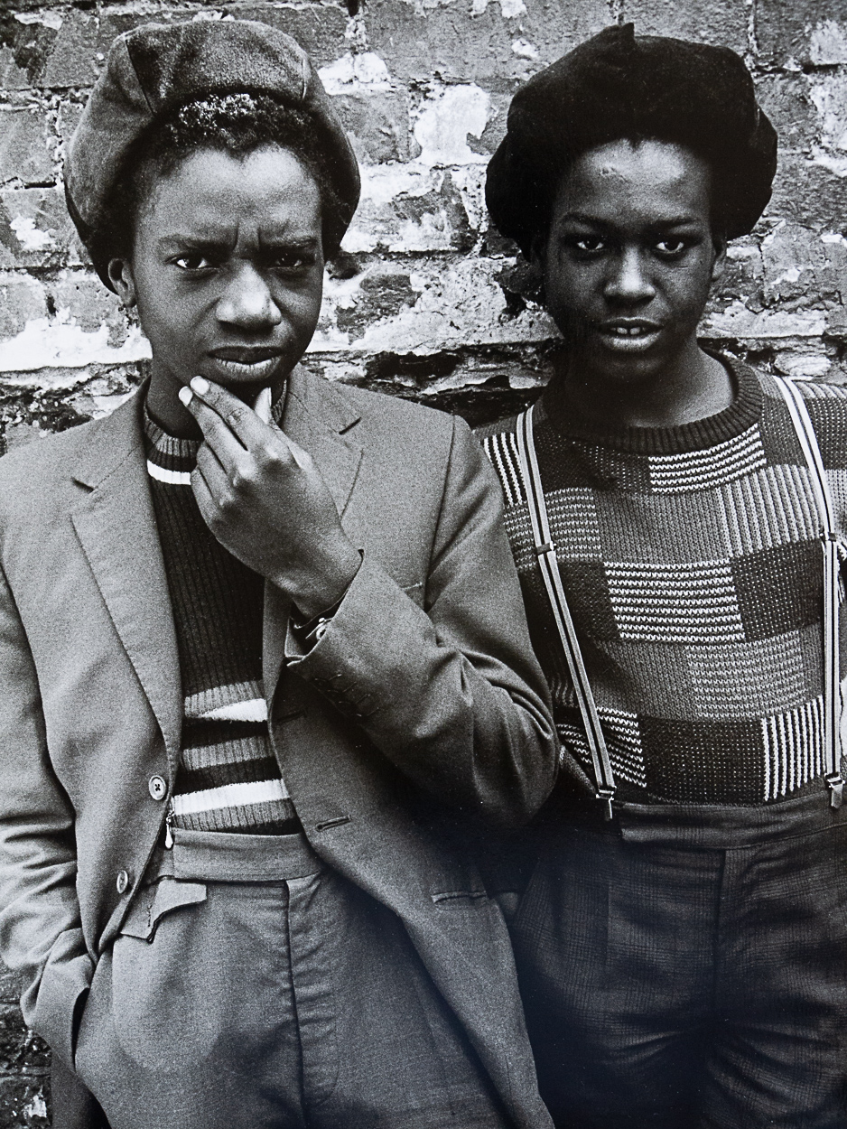 Two young women standing next to each other in front of a brick wall.
