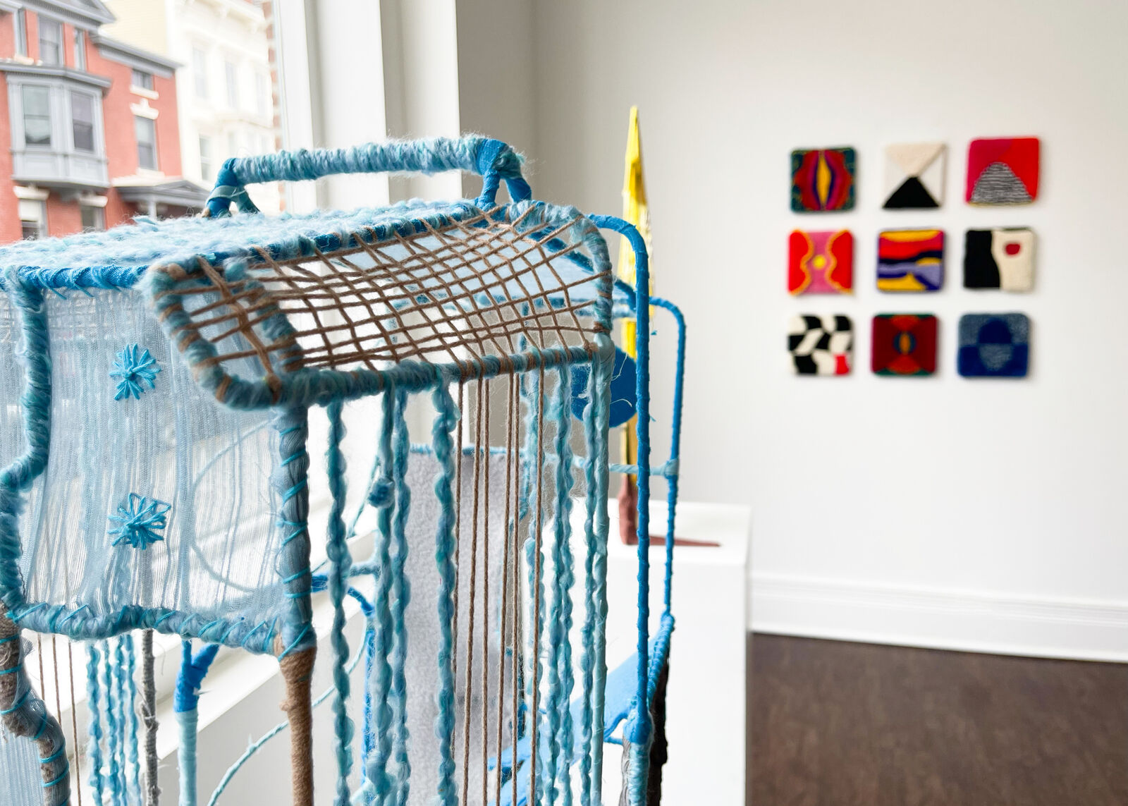 A woven, cage-like sculpture featuring blue and brown yarns with a stylized figure silhouette.