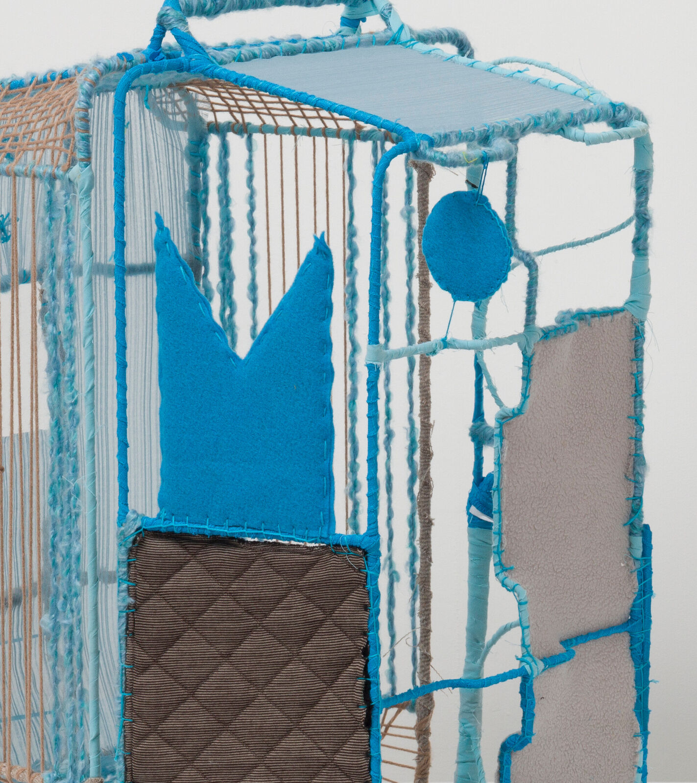 A woven, cage-like sculpture featuring blue and brown yarns with a stylized figure silhouette.
