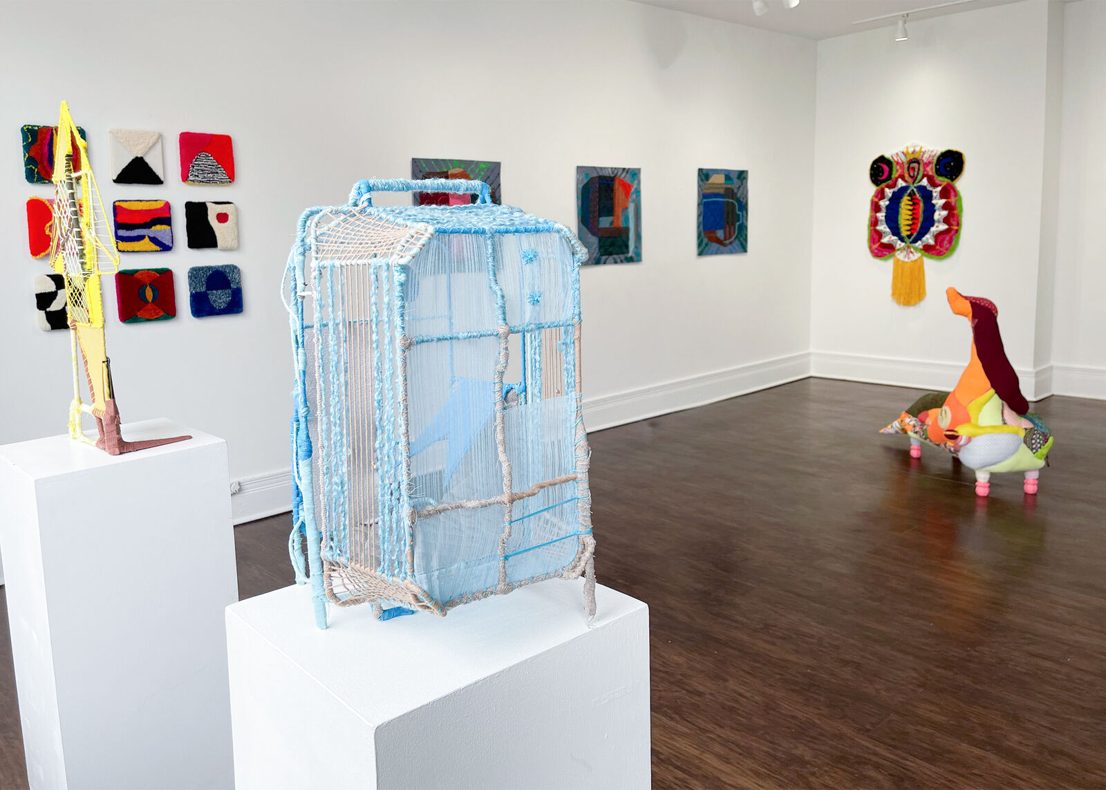 A geometric textile sculpture resembling a stylized house or sailboat, constructed from yellow and brown yarns.