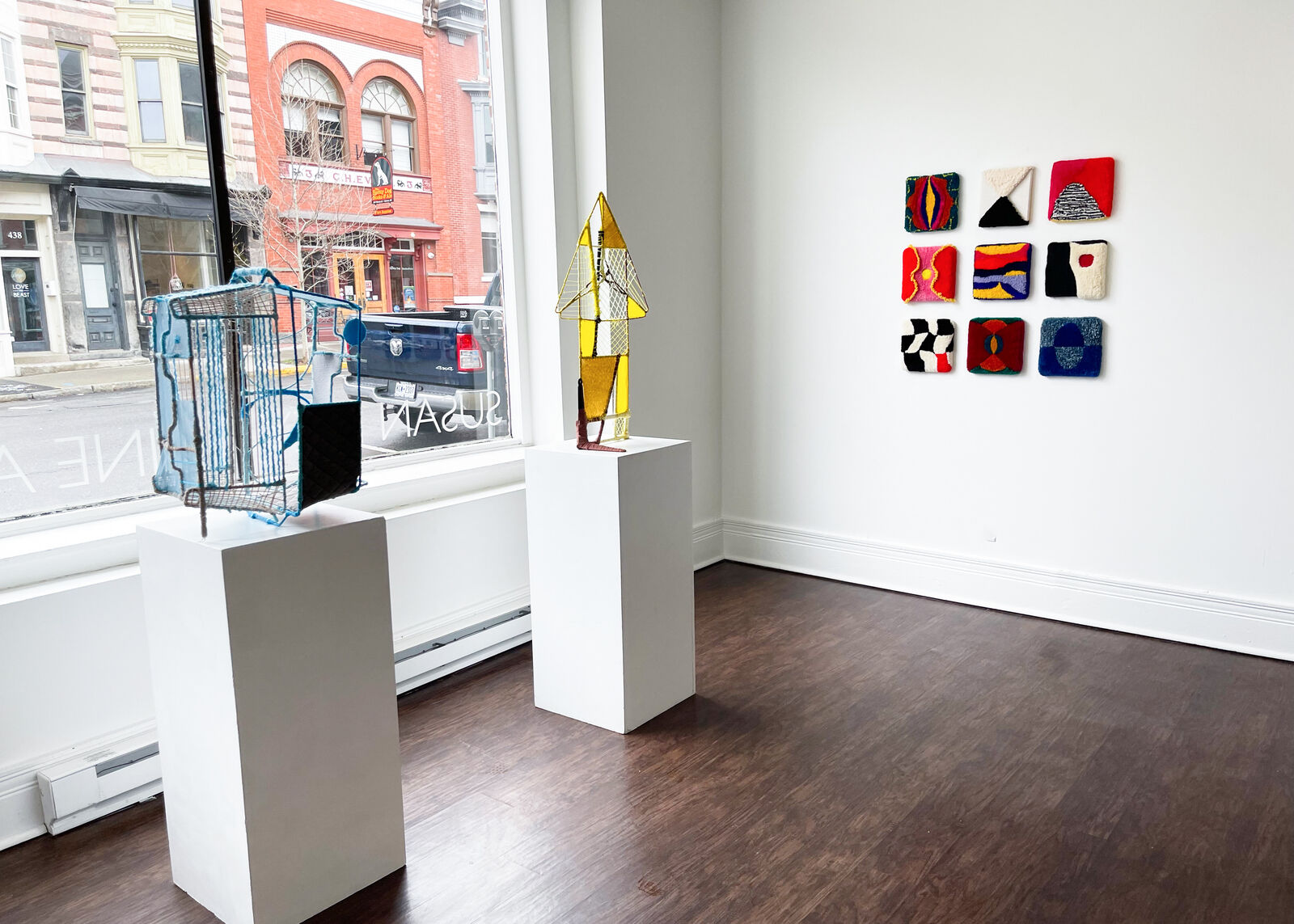 A geometric textile sculpture resembling a stylized house or sailboat, constructed from yellow and brown yarns.