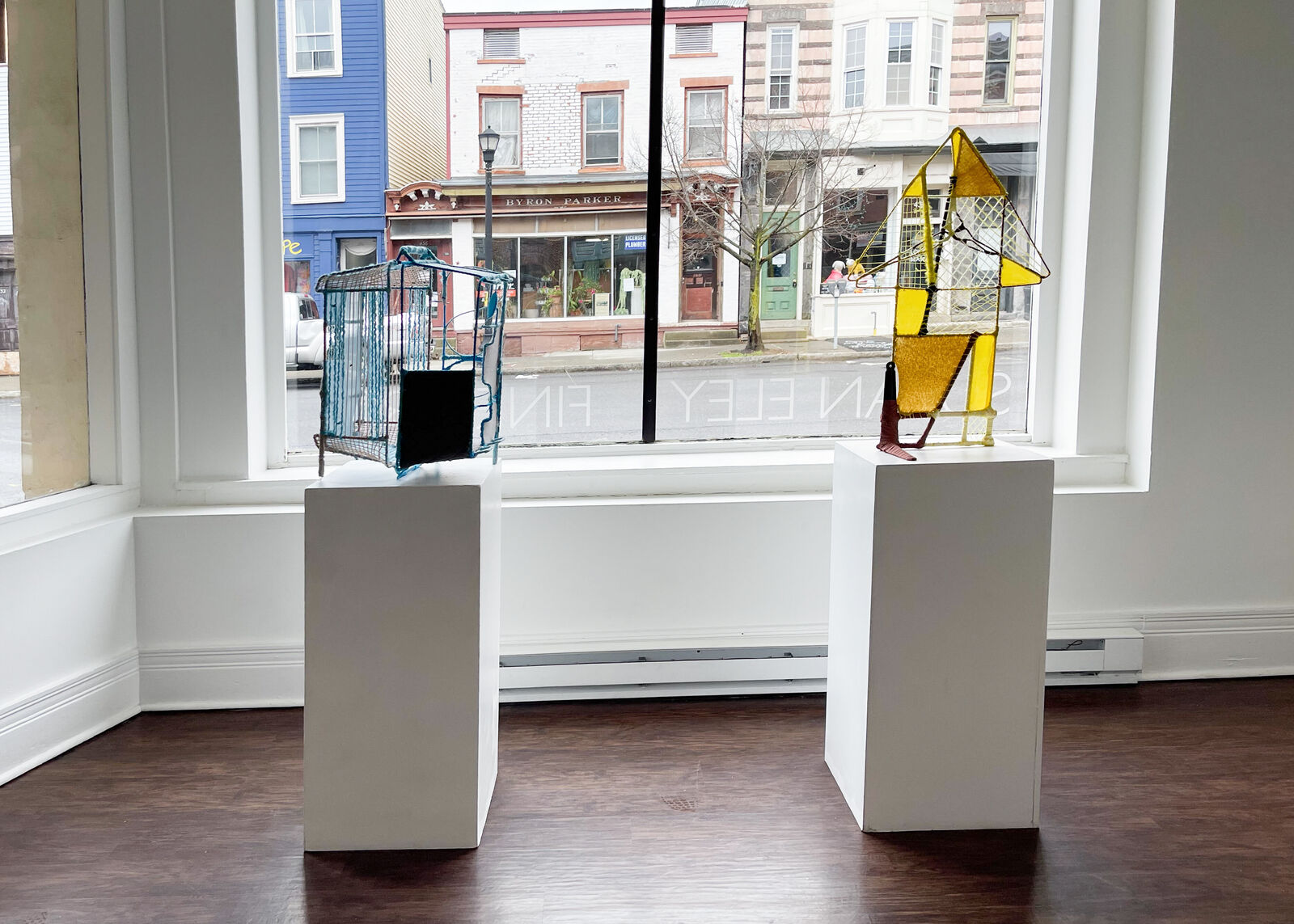 A geometric textile sculpture resembling a stylized house or sailboat, constructed from yellow and brown yarns.