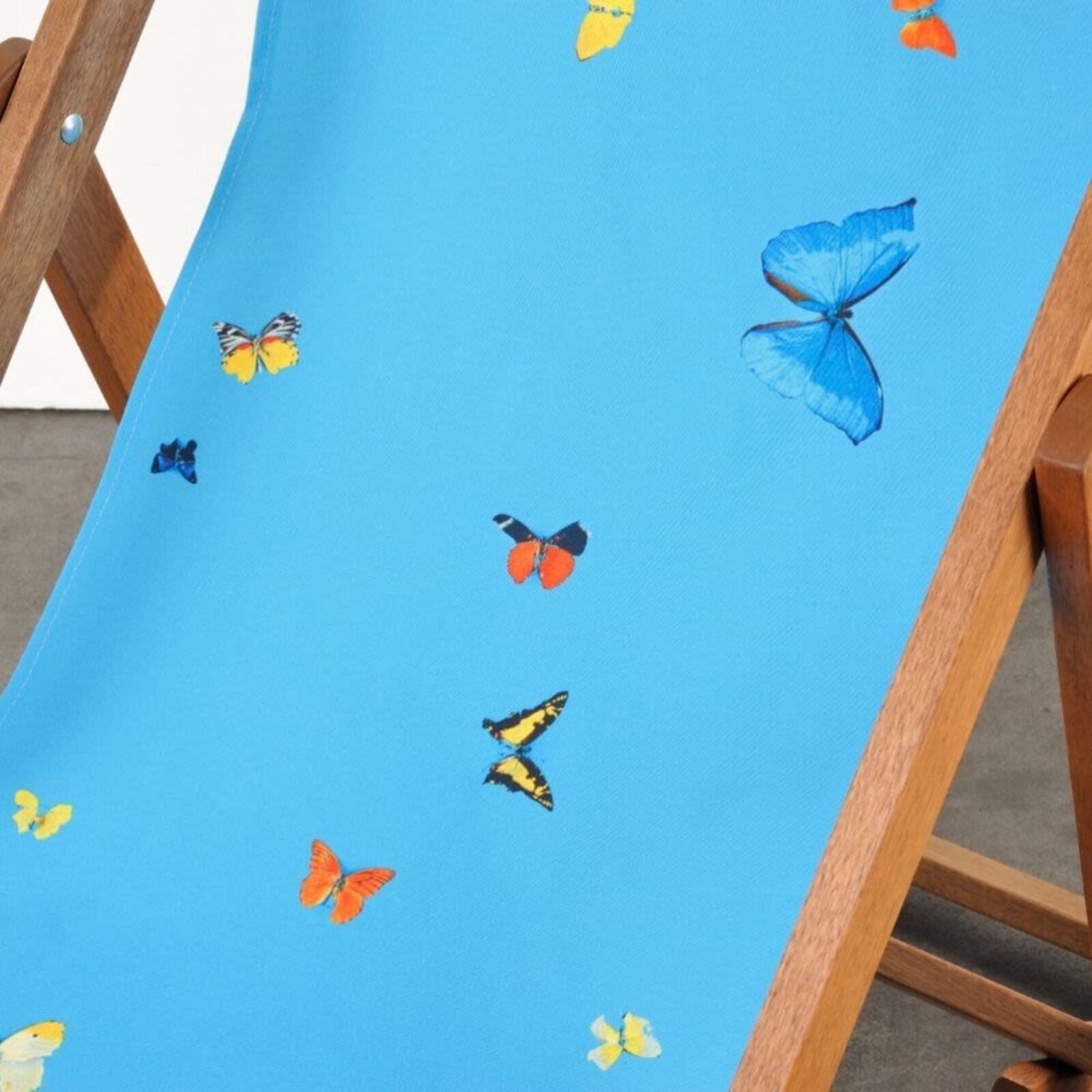 A wooden deck chair with a blue butterfly print on it.