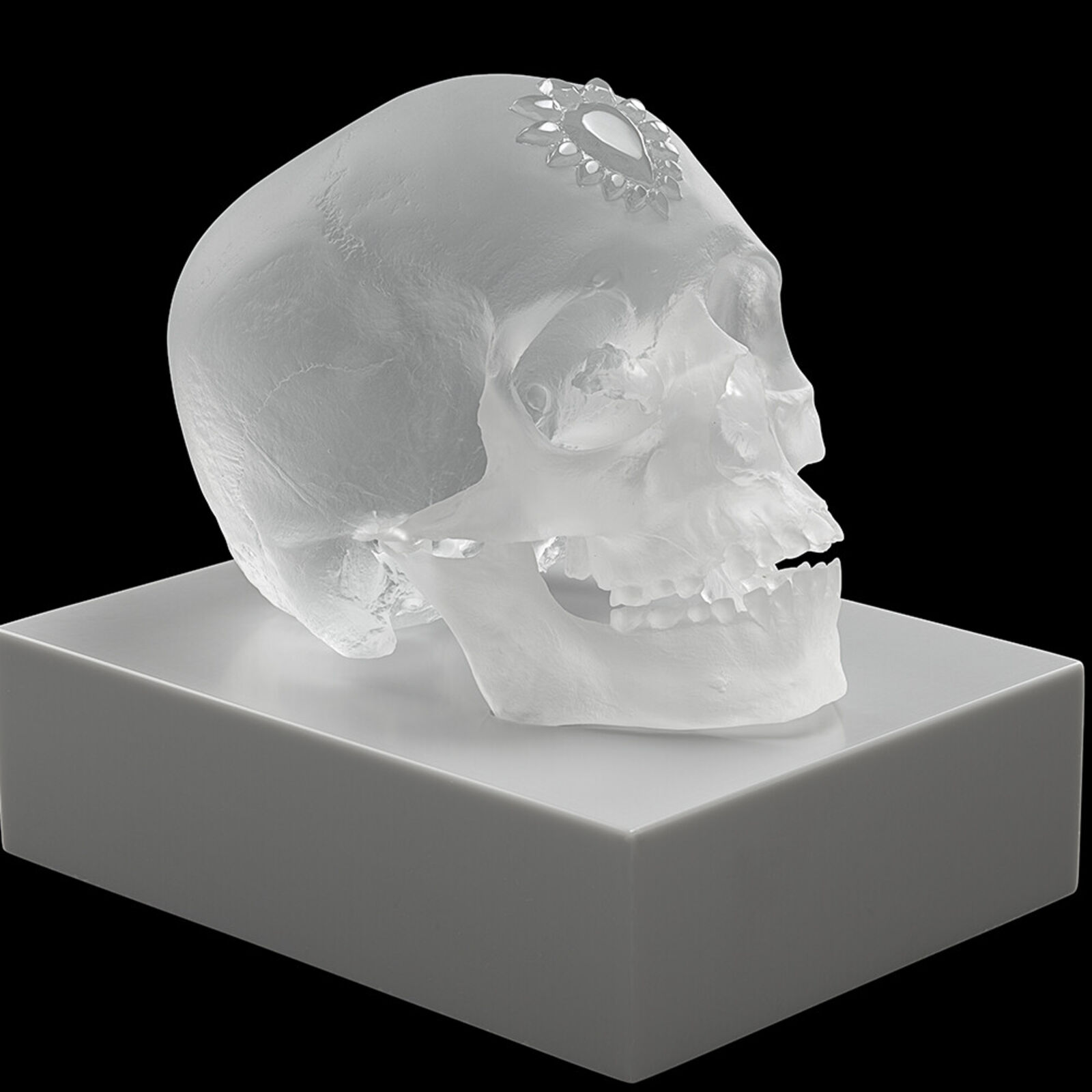 A clear glass skull on a white pedestal with a black background.