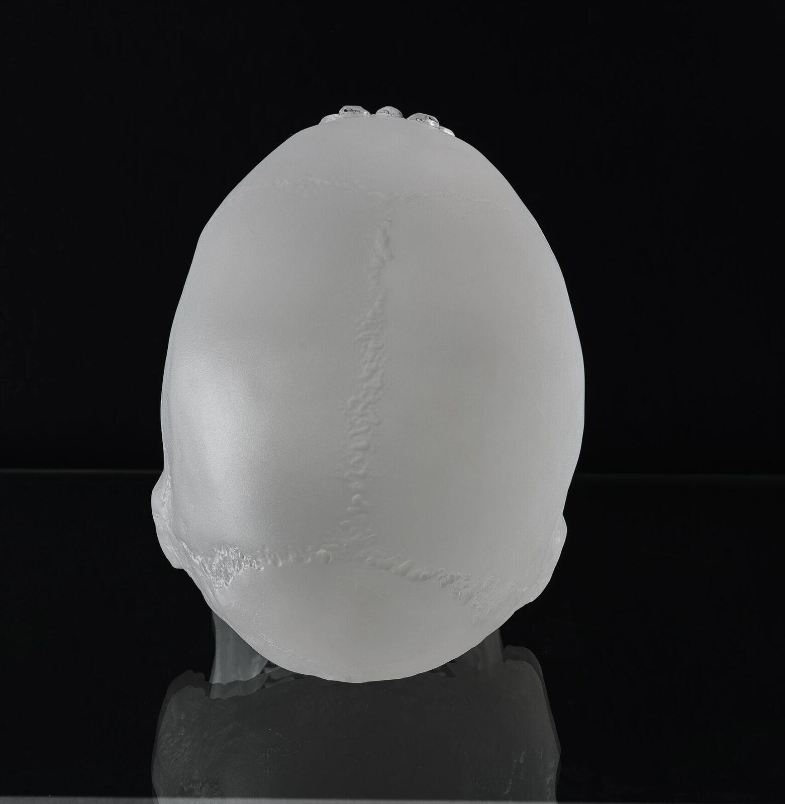 A clear glass skull on a white pedestal with a black background.
