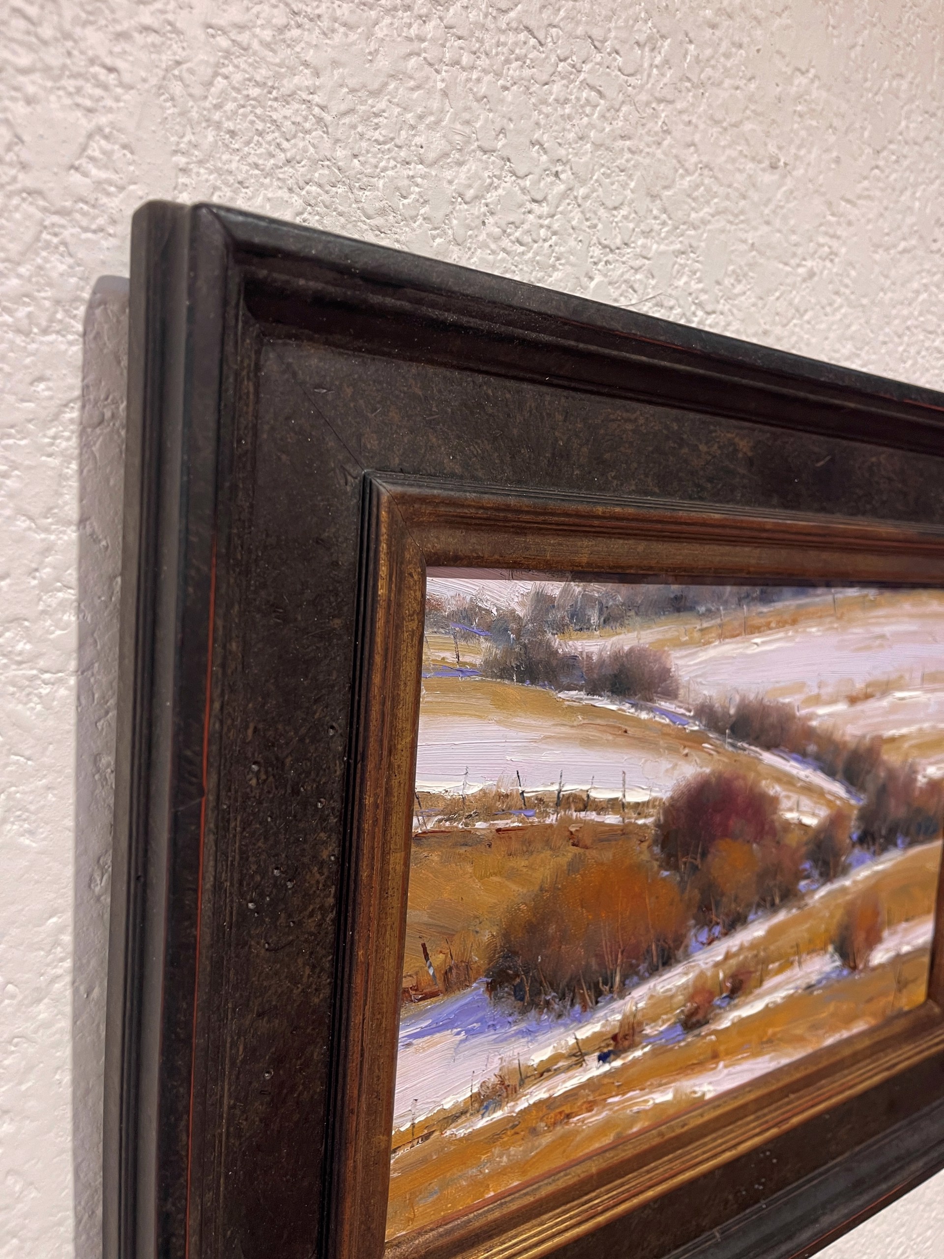 A winter landscape painting featuring snow-covered hills and dark shrubs.