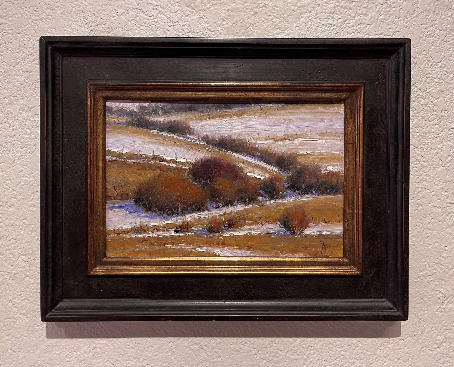 A winter landscape painting featuring snow-covered hills and dark shrubs.