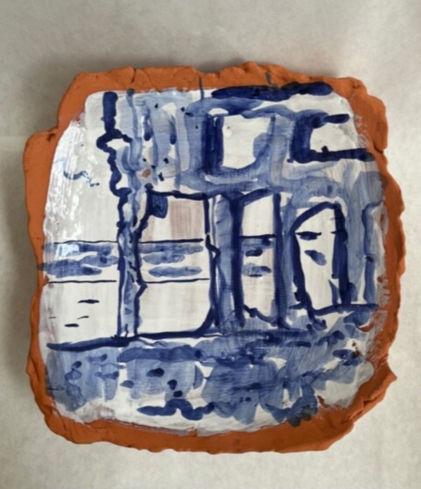 A hand-painted clay tile featuring a blue architectural sketch against an orange rim.