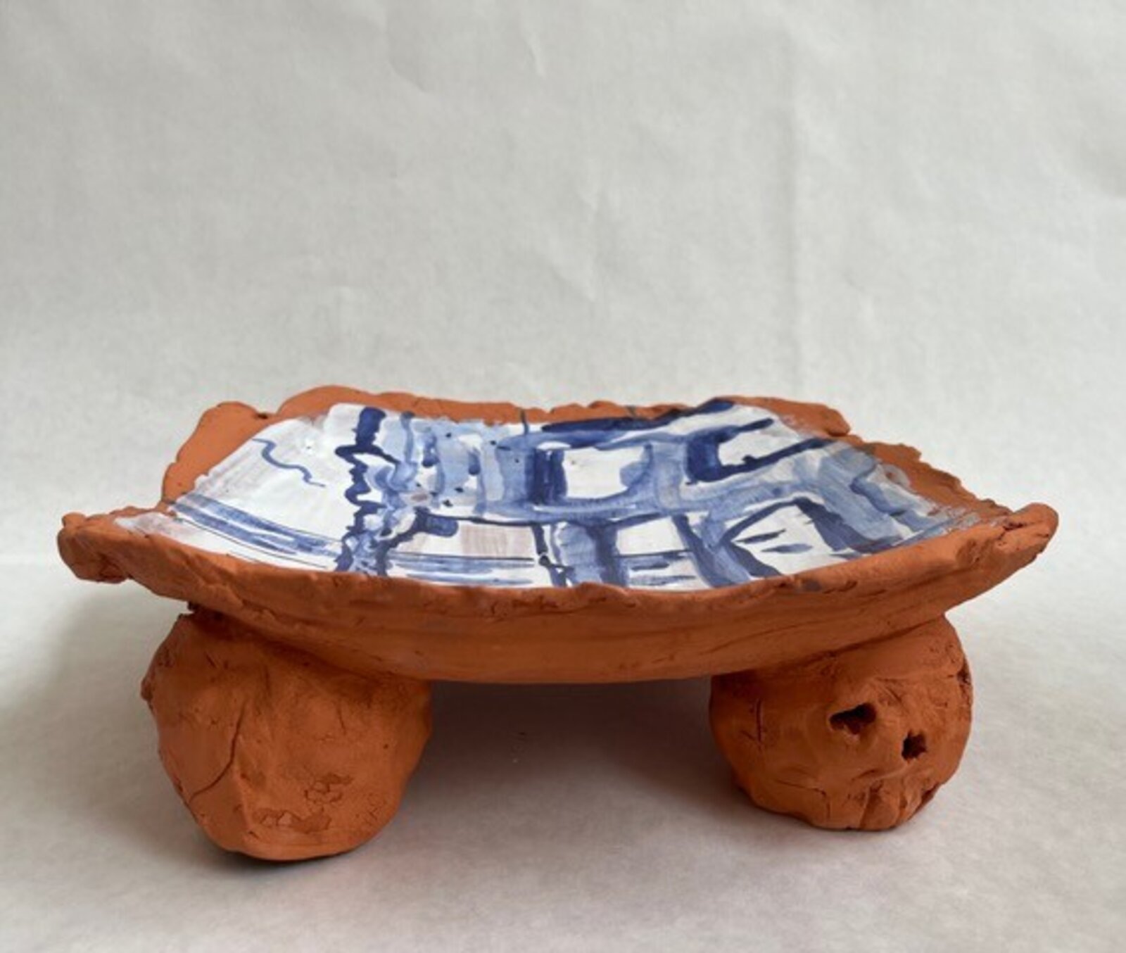 A hand-painted clay tile featuring a blue architectural sketch against an orange rim.