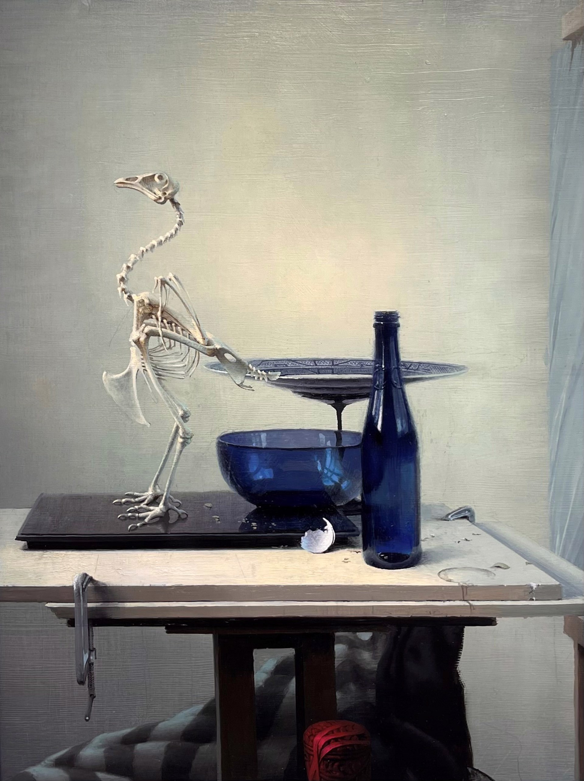 A surreal still life featuring a bird skeleton, blue glassware, and a bottle on a table.