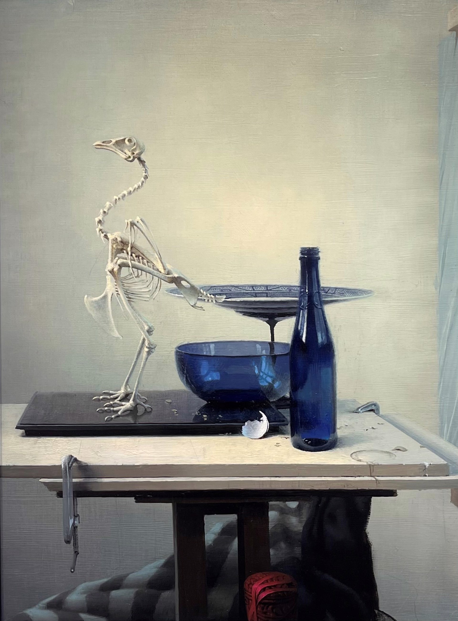 A surreal still life featuring a bird skeleton, blue glassware, and a bottle on a table.