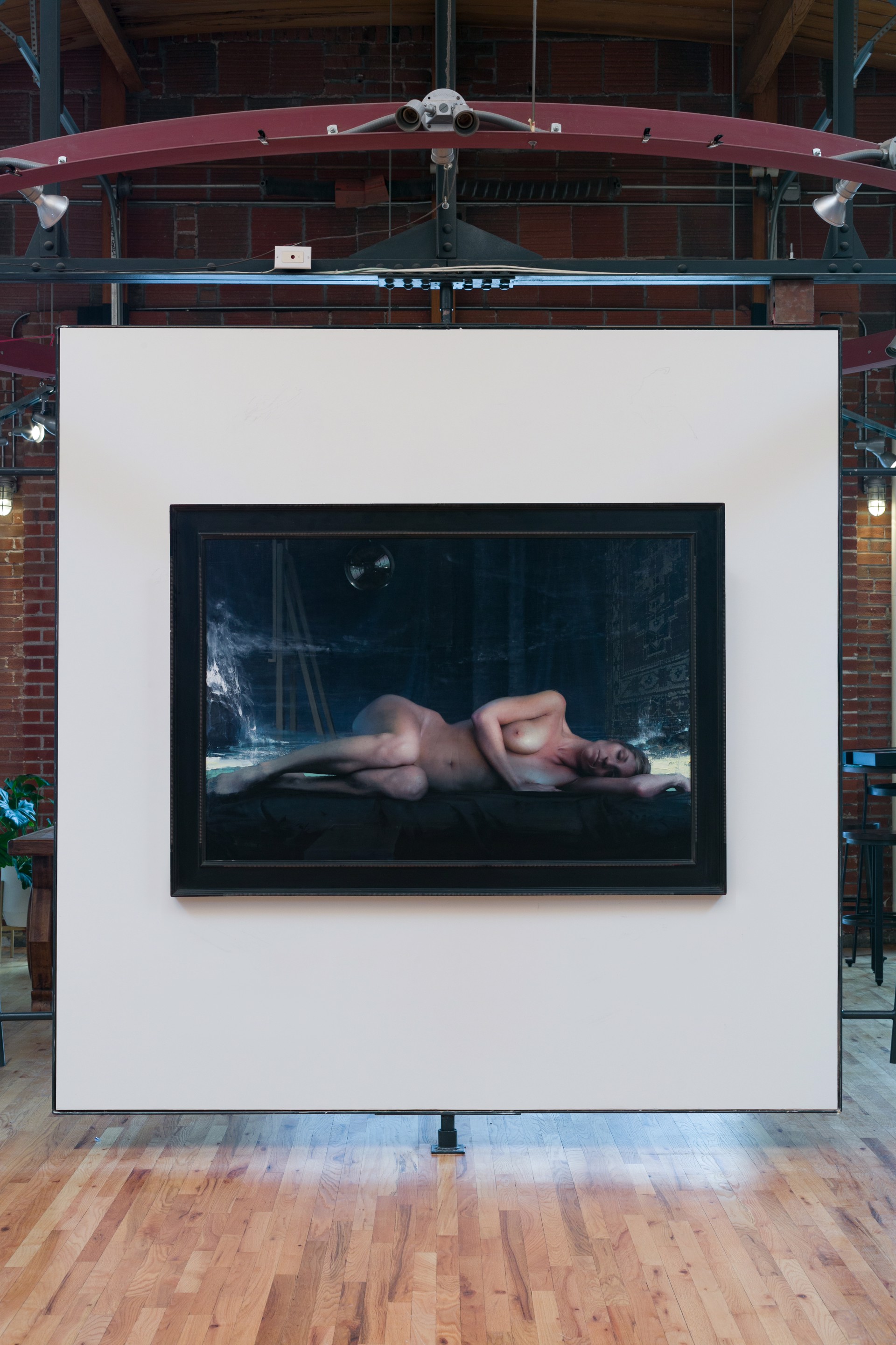 A nude figure lies on a dark surface in a dimly lit, atmospheric scene.