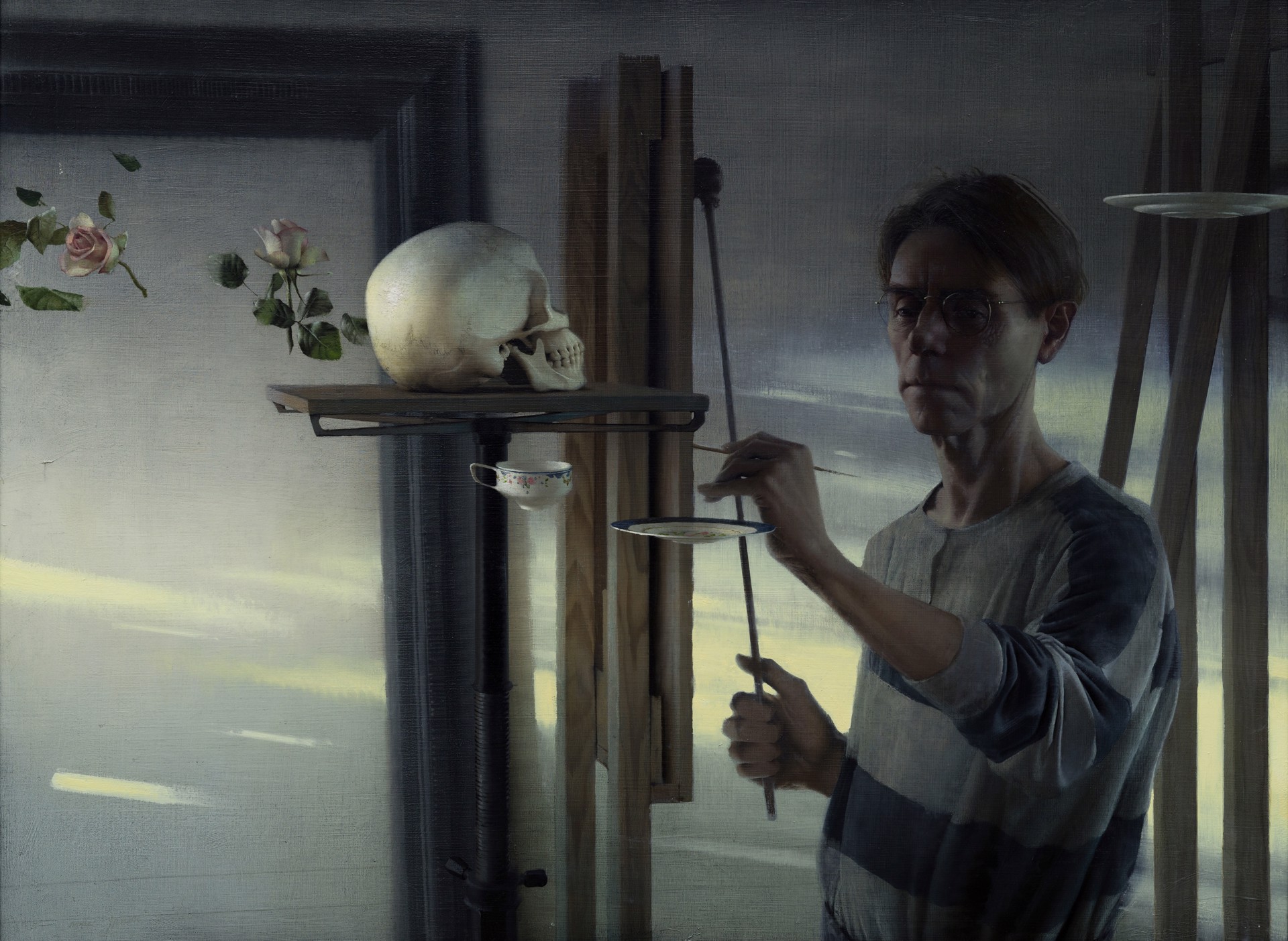 A painter in a studio works on a still life featuring a skull and delicate flowers.
