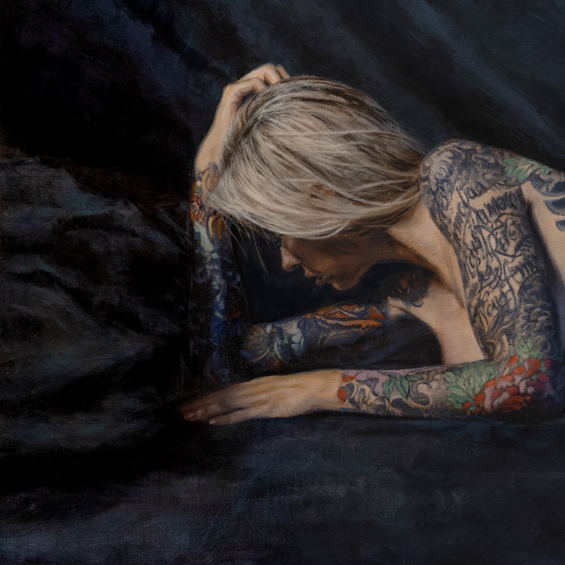A figure with extensive colorful tattoos lies prone on a dark surface.